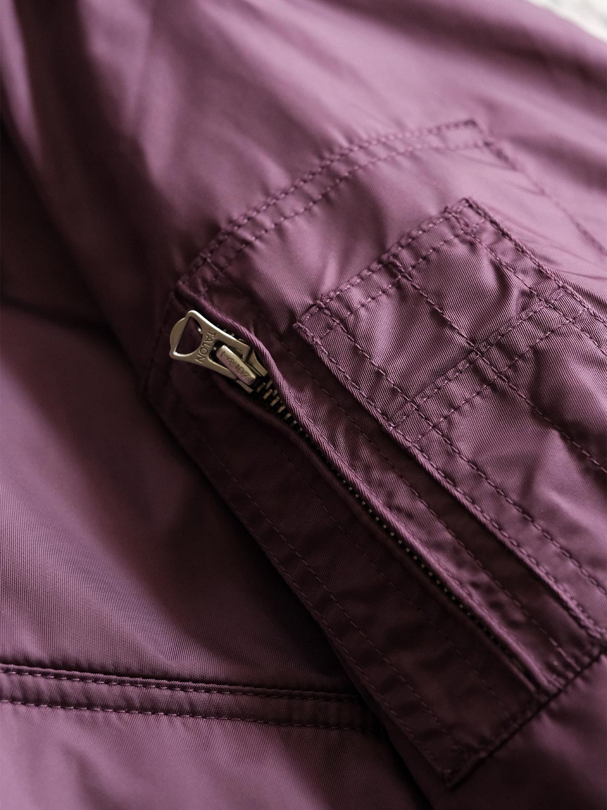 製品画像:
CWU-45Pフライトジャケットの全体展示。高密度ナイロン外層と厚手のキルティング綿を使用した、保温性と防風性に優れたクラシックなフライトジャケットの全体像。
詳細画像:
TALONメタルジッパーとマジックテープエンブレムのディテール。フラップポケットやリブ編みの袖口、裾など、ミリタリーウェア特有のデザインが強調された画像。