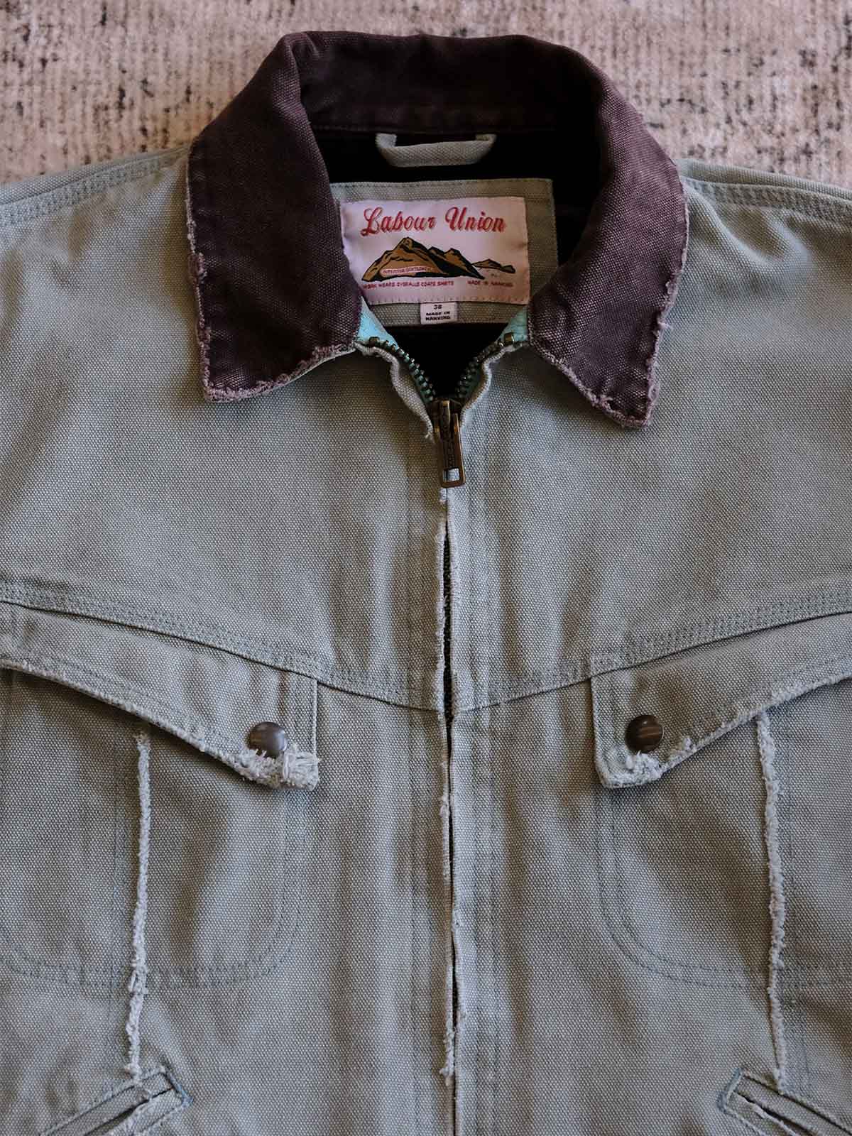 製品画像:
リバイバルダメージパッチワークキャンバスジャケット全体展示。15ozの定織キャンバスと日本製厚ウール裏地を使用し、ヴィンテージスタイルを引き立てるタフなキャンバスジャケットの全体像。
詳細画像:
TALONジッパー、スナップボタン、及び水洗い加工のディテール。多重水洗い加工と手作業のダメージ加工が施された、ヴィンテージ感が強調されたディテール。