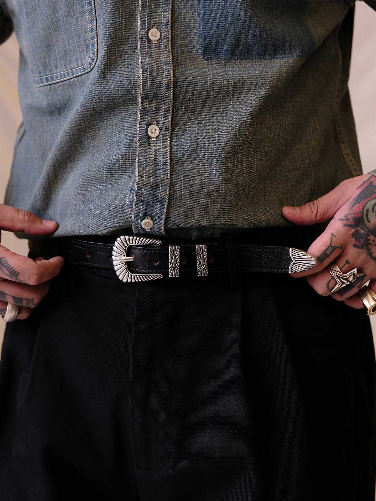 詳細画像:
エッチング加工された真鍮バックルのディテール。精緻な彫刻が施された立体感のあるバックルが、ヴィンテージスタイルの魅力を引き立てるディテール。
モデル画像:
モデルがヴィンテージキャバルリーベルトを着用し、デニムやカーゴパンツと合わせて、アメリカンウェスタンスタイルを披露している画像。