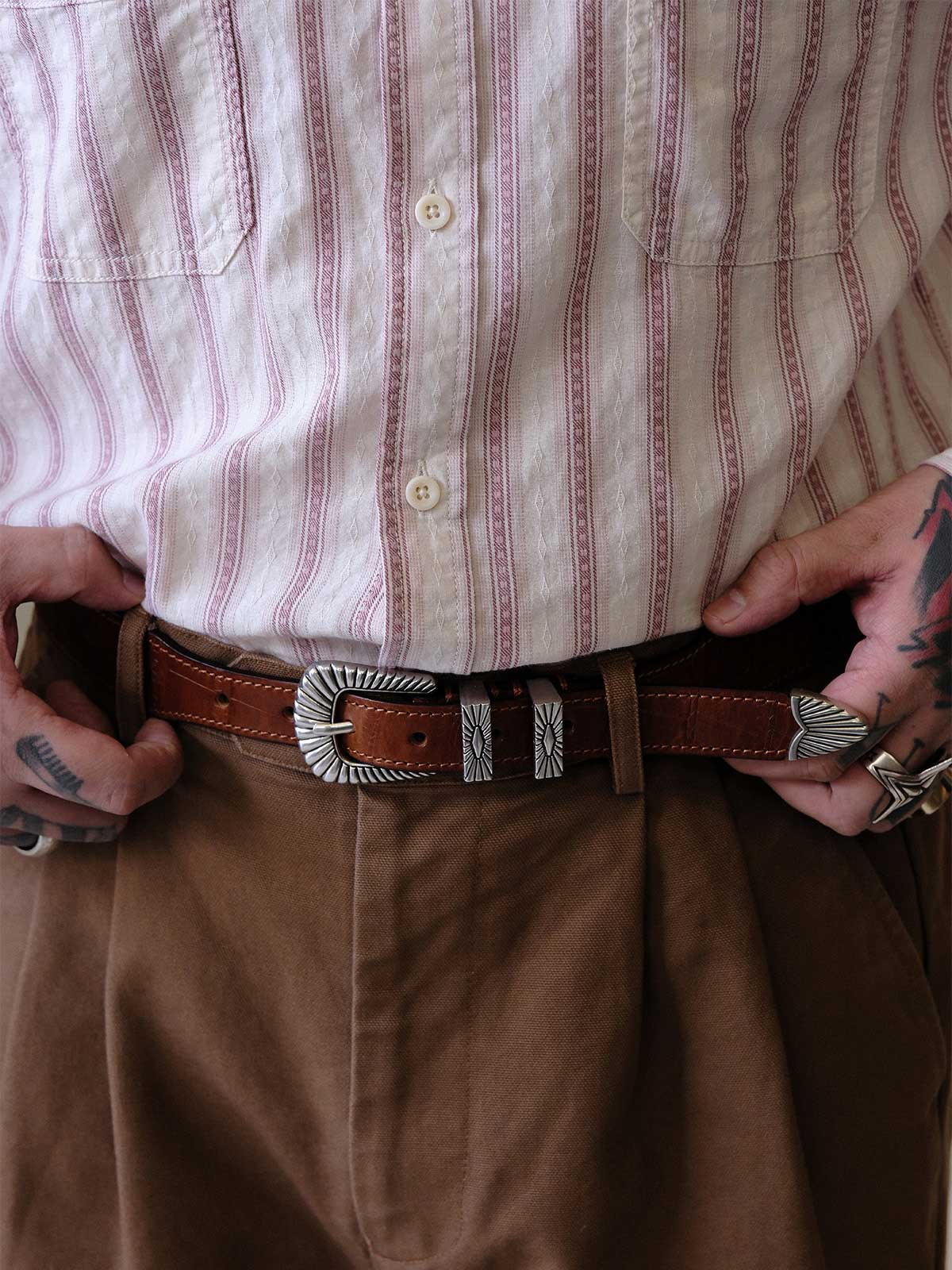 詳細画像:
エッチング加工された真鍮バックルのディテール。精緻な彫刻が施された立体感のあるバックルが、ヴィンテージスタイルの魅力を引き立てるディテール。
モデル画像:
モデルがヴィンテージキャバルリーベルトを着用し、デニムやカーゴパンツと合わせて、アメリカンウェスタンスタイルを披露している画像。