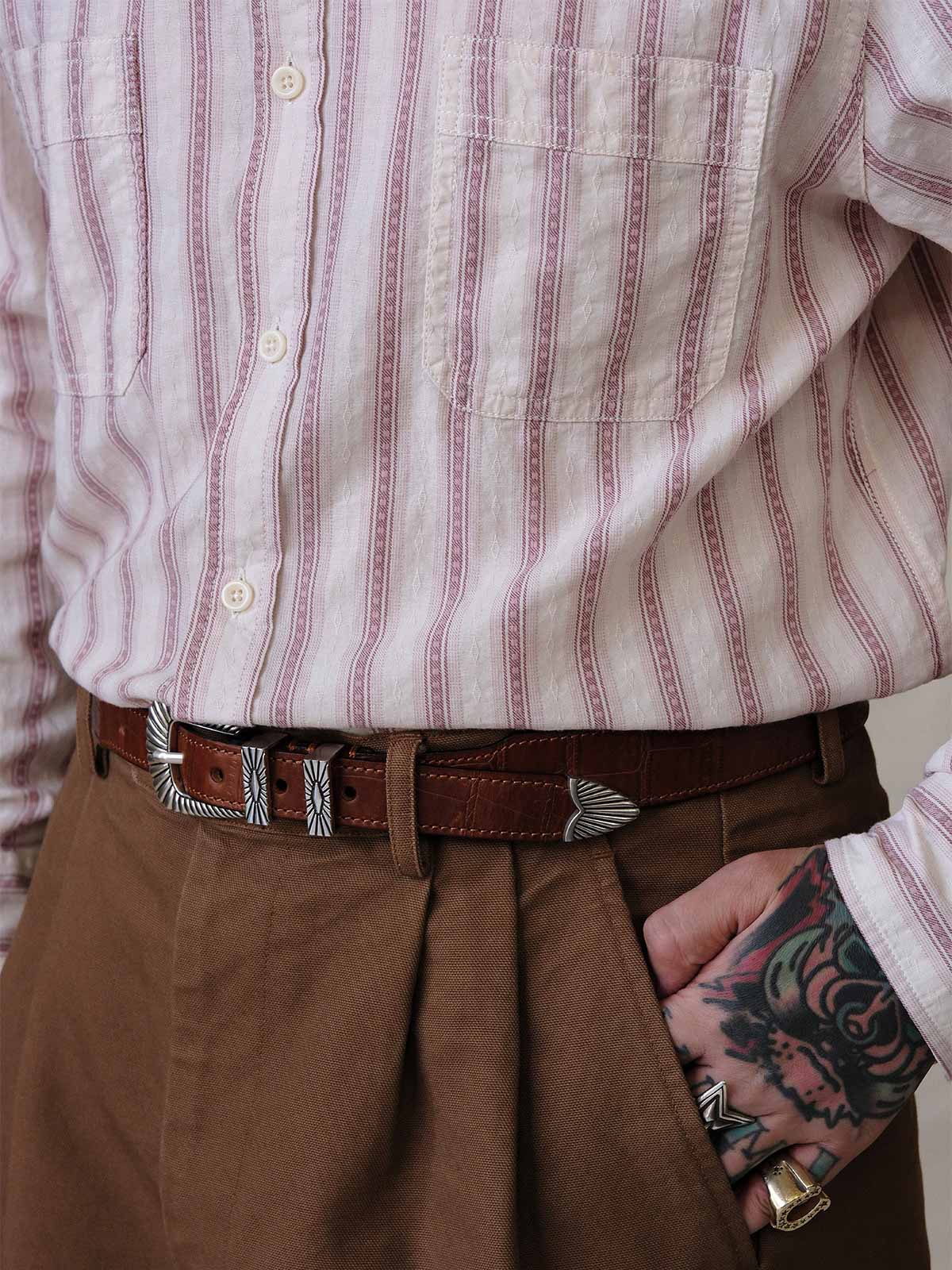 詳細画像:
エッチング加工された真鍮バックルのディテール。精緻な彫刻が施された立体感のあるバックルが、ヴィンテージスタイルの魅力を引き立てるディテール。
モデル画像:
モデルがヴィンテージキャバルリーベルトを着用し、デニムやカーゴパンツと合わせて、アメリカンウェスタンスタイルを披露している画像。