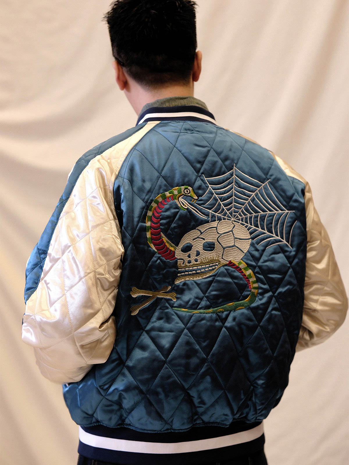 詳細画像:
精緻な刺繍と光沢サテン生地のディテール。大面積の刺繍デザインと鮮やかな色合いが、ジャケットに強い視覚的インパクトを与えるディテール。
モデル画像:
モデルがスカジョンジャケットを着用し、ジーンズやカーゴパンツと合わせて、クラシックなヴィンテージスタイルを披露している画像。