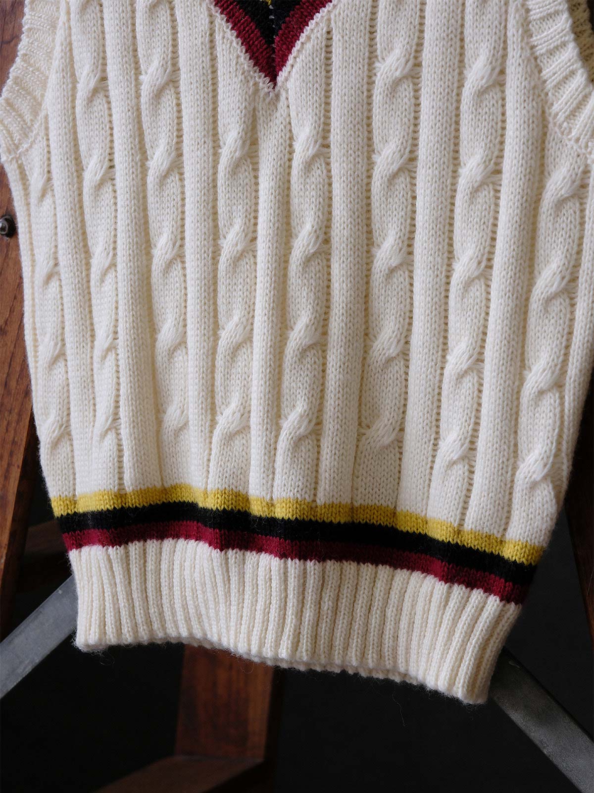 製品画像:
アカデミックスタイルVネック クリケットニットベストの全体展示。クラシックなツイスト編みとストライプデザインが特徴的な、100%ウール素材を使用したVネックデザインのニットベスト。
詳細画像:
ツイスト編みの編み目とカラーコンビネーションストライプのディテール。Vネックとストライプデザインが加える視覚的なレイヤード感を強調した画像。