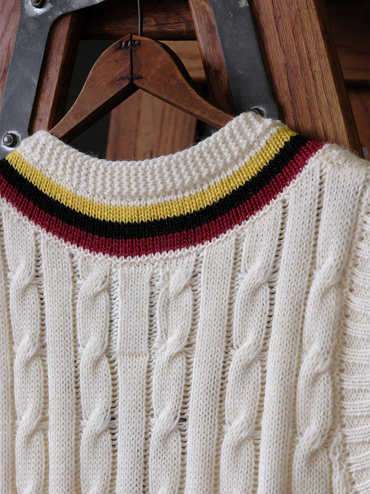 製品画像:
アカデミックスタイルVネック クリケットニットベストの全体展示。クラシックなツイスト編みとストライプデザインが特徴的な、100%ウール素材を使用したVネックデザインのニットベスト。
詳細画像:
ツイスト編みの編み目とカラーコンビネーションストライプのディテール。Vネックとストライプデザインが加える視覚的なレイヤード感を強調した画像。