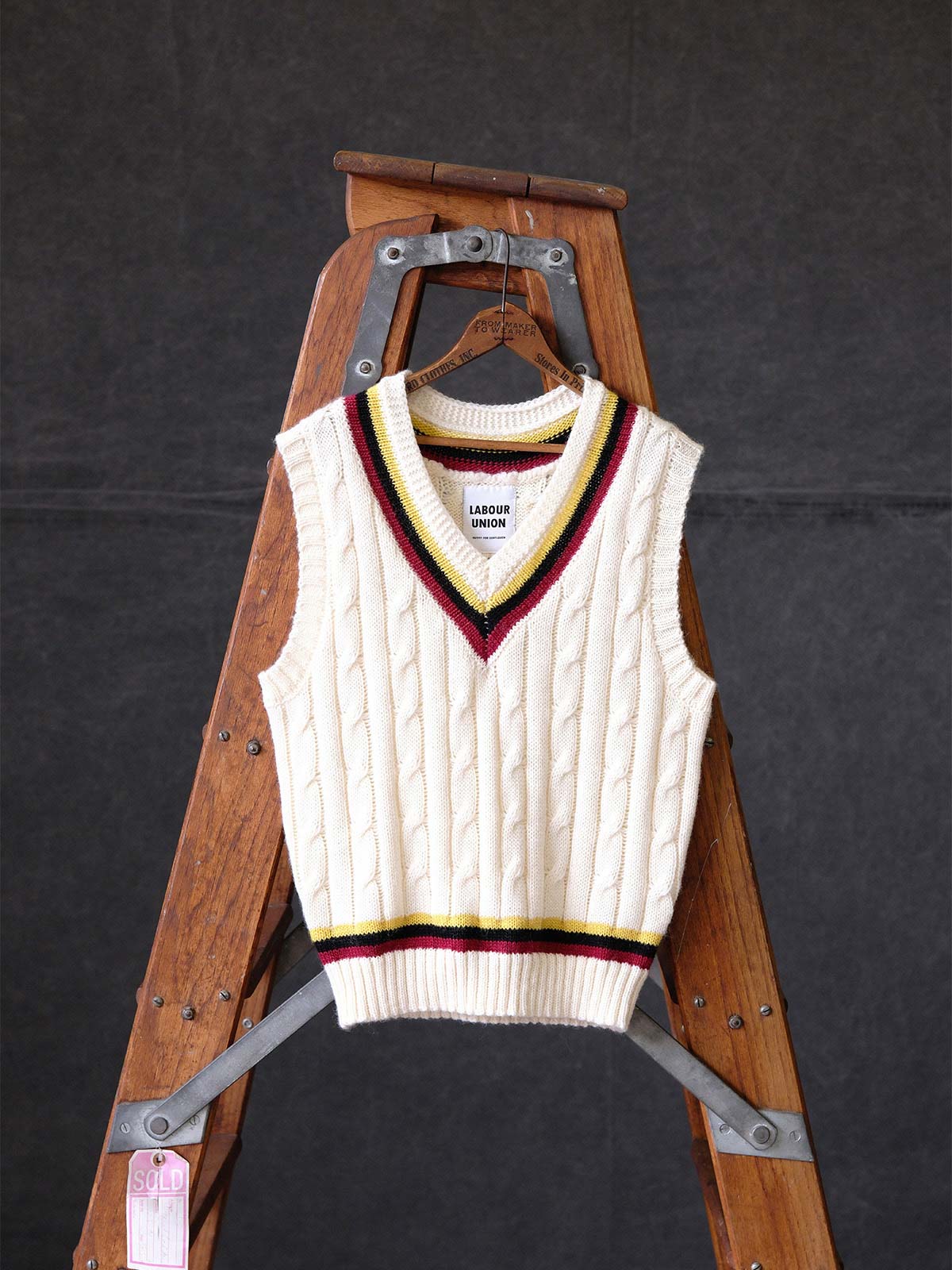 製品画像:
アカデミックスタイルVネック クリケットニットベストの全体展示。クラシックなツイスト編みとストライプデザインが特徴的な、100%ウール素材を使用したVネックデザインのニットベスト。
詳細画像:
ツイスト編みの編み目とカラーコンビネーションストライプのディテール。Vネックとストライプデザインが加える視覚的なレイヤード感を強調した画像。