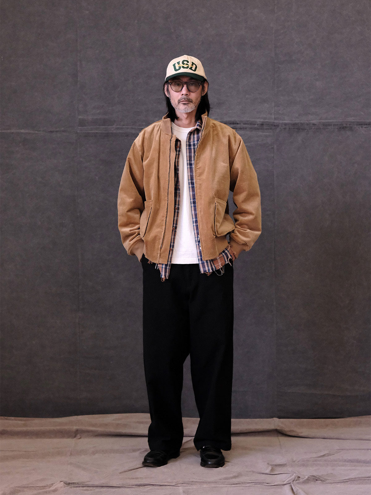 詳細画像:
リブ編みの襟、袖口、裾とプリーツデザインのディテール。寒風を防ぎ、自由な動きをサポートする機能的なデザインとミリタリー感が引き立ちます。
モデル画像:
モデルがコーデュロイ×ウール ミリタリージャケットを着用し、ミリタリースタイルのワークパンツと合わせてヴィンテージ軍旅風を披露。