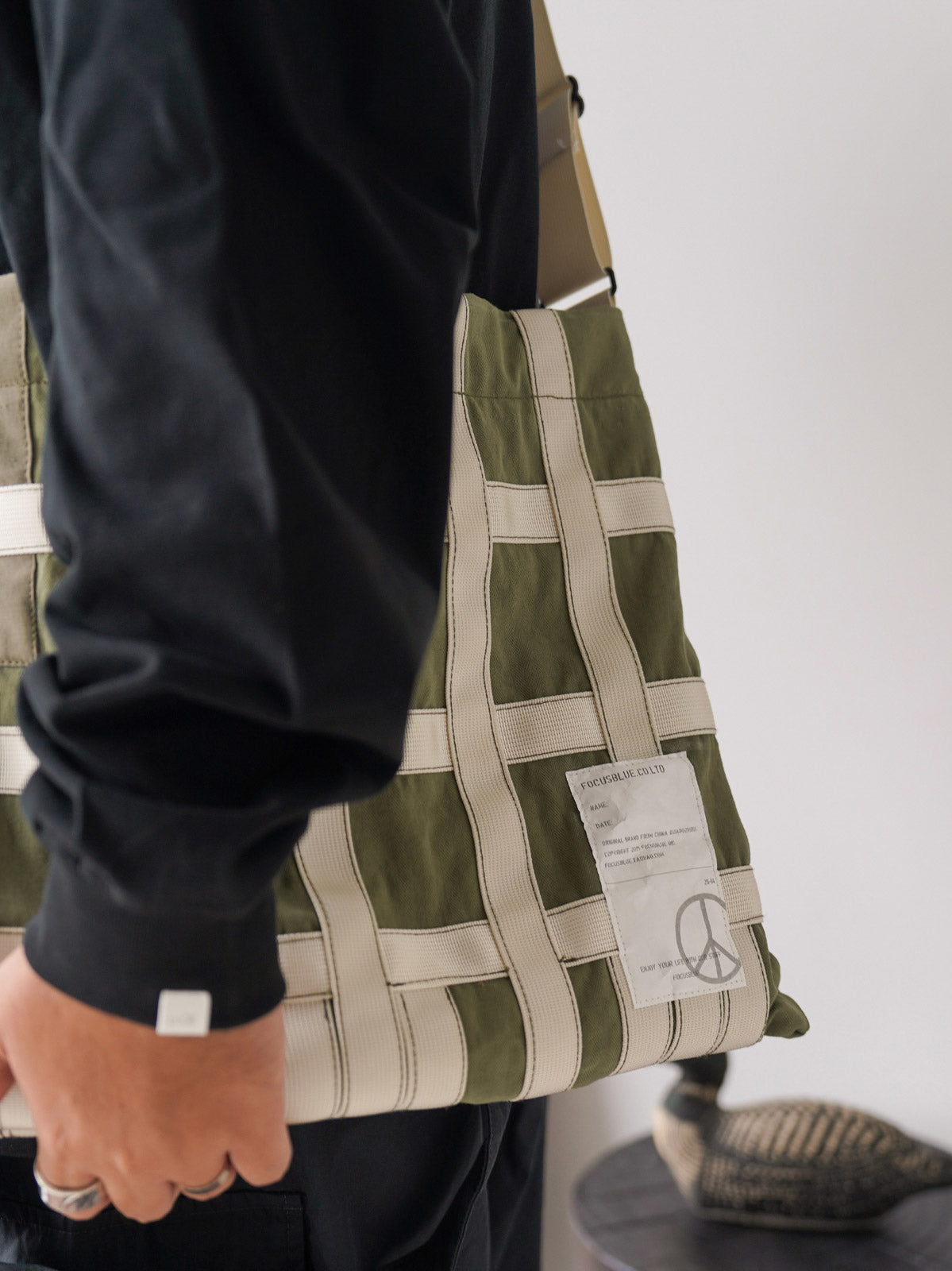 製品画像: ミリタリーテイストのショルダーバッグの全体展示
詳細画像: テントファブリックとウェビングのディテール
モデル画像: モデルが着用したミリタリーショルダーバッグのスタイリング例