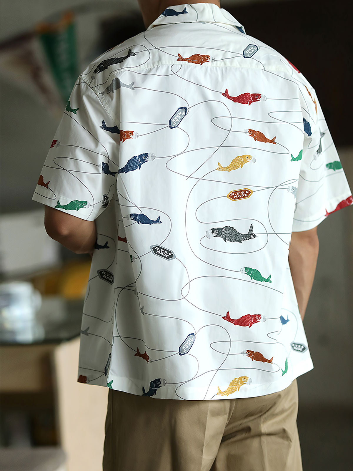 モデルが鯉プリントのハワイアンシャツを着用し、夏のカジュアルスタイルを披露。