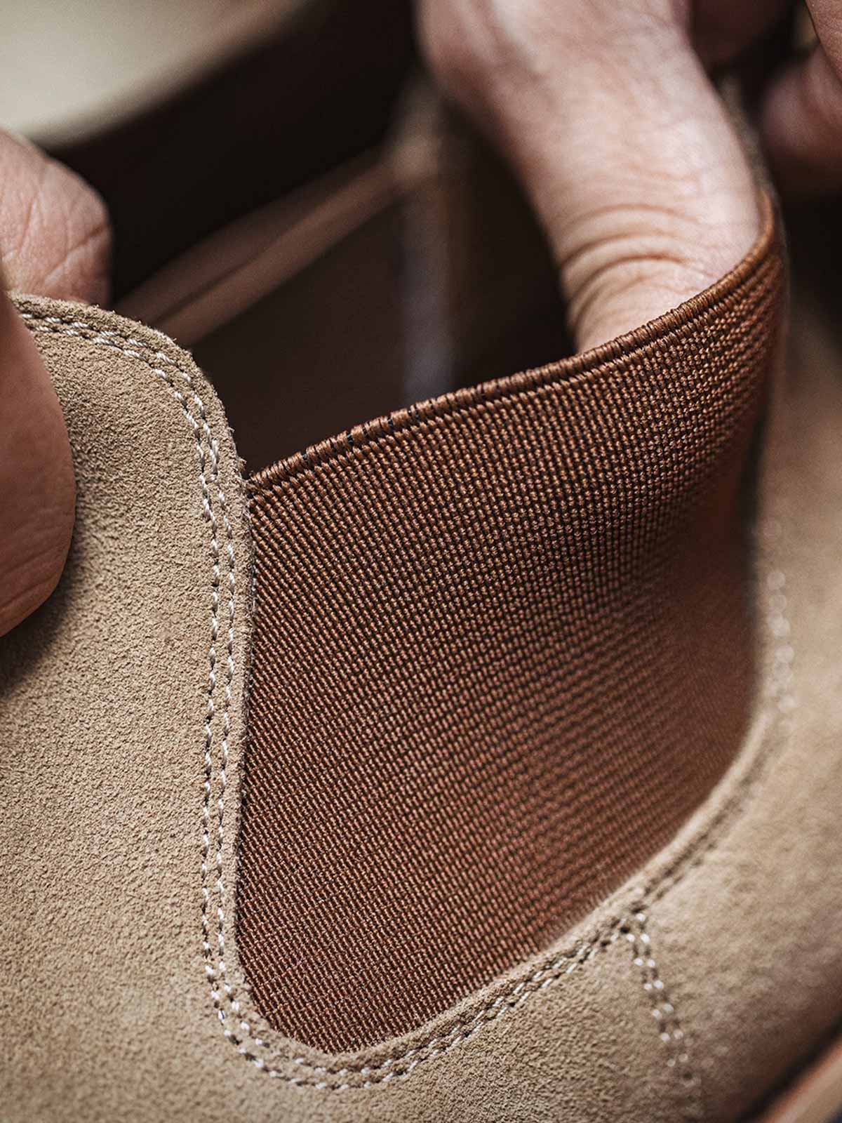 製品画像:
ライトブラウンのスエードチェルシーブーツ全体画像。シンプルで洗練されたデザインが特徴で、秋冬シーズンに最適なスタイルを提案します。

詳細画像:
チェルシーブーツのゴムバンドとスエードの質感がクローズアップされたディテール画像。履きやすさとデザインの美しさが強調されています。