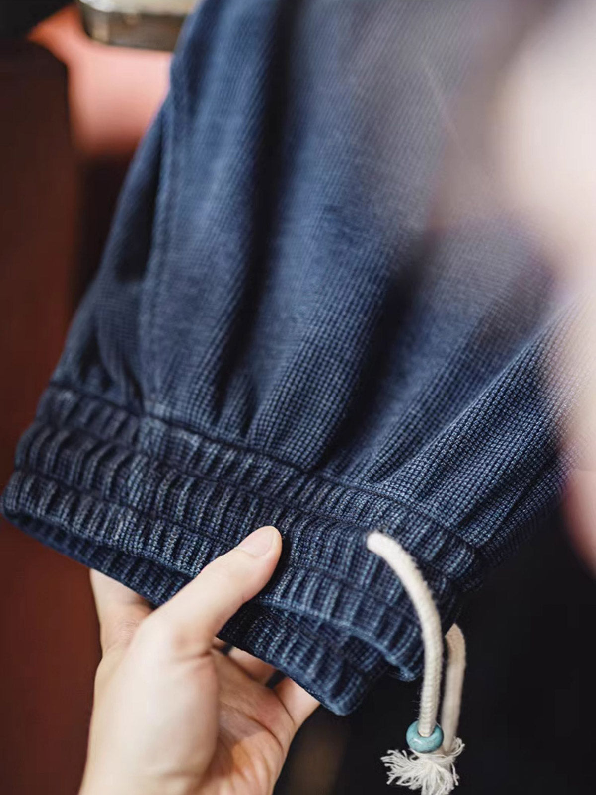 製品画像: ワッフルニットドレープ効果付きカジュアルパンツ正面図
詳細画像: パンツのディテール、白い編み込みドローストリングと石風ビーズ