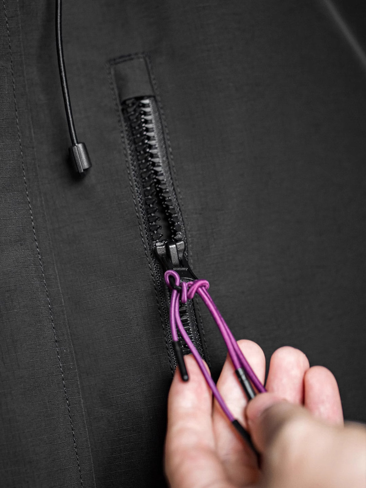 製品画像: 三つポケット撥水性フード付きテクニカルジャケット 正面、アウトドアから都市通勤まで対応
詳細画像: グロメットジッパーとレインシェルデザインのディテール、防護性能