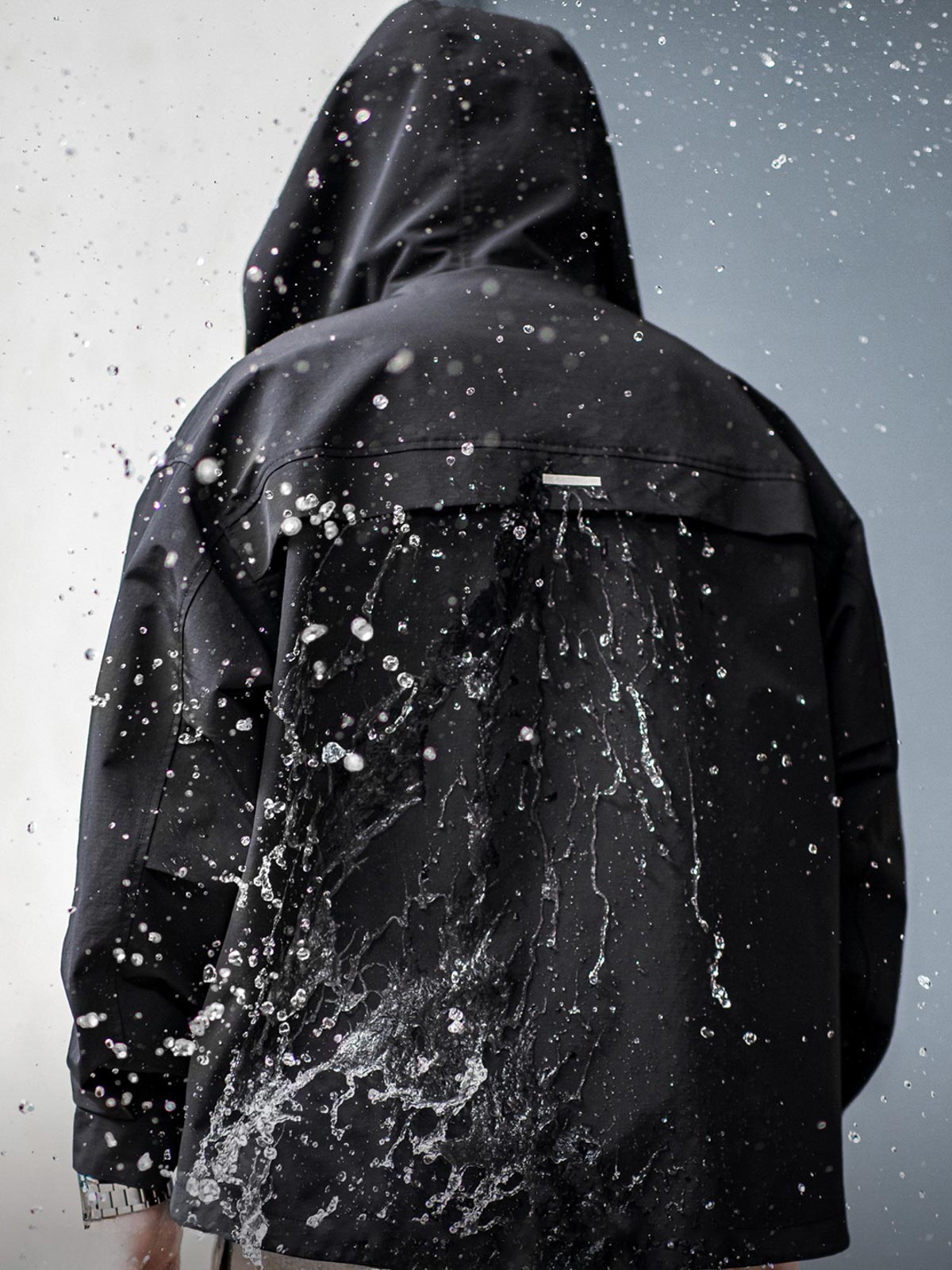 製品画像: 三つポケット撥水性フード付きテクニカルジャケット 正面、アウトドアから都市通勤まで対応
詳細画像: グロメットジッパーとレインシェルデザインのディテール、防護性能