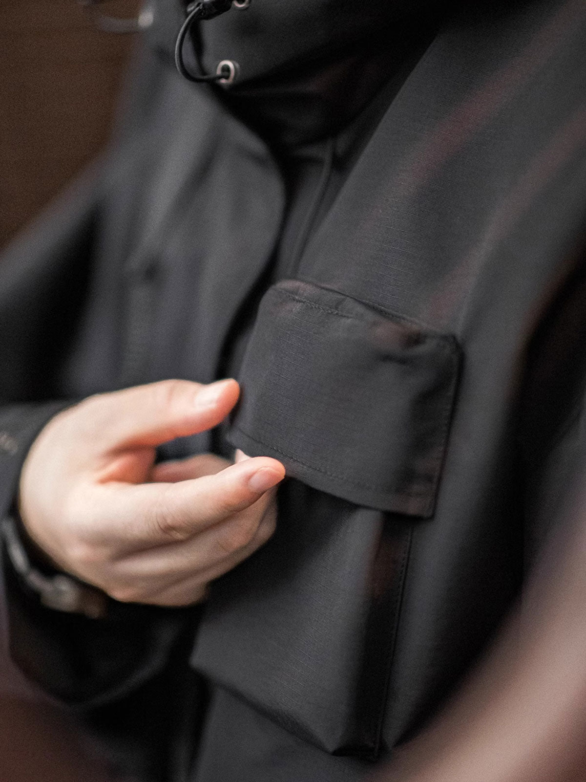 製品画像: 三つポケット撥水性フード付きテクニカルジャケット 正面、アウトドアから都市通勤まで対応
詳細画像: グロメットジッパーとレインシェルデザインのディテール、防護性能