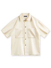 透明感のある竹節平織りテクスチャのオーバーサイズ半袖シャツの正面ビュー。リラックスフィットでエレガントなドレープを特徴とし、実用的な大型スクエアポケットがデザインアクセントです。