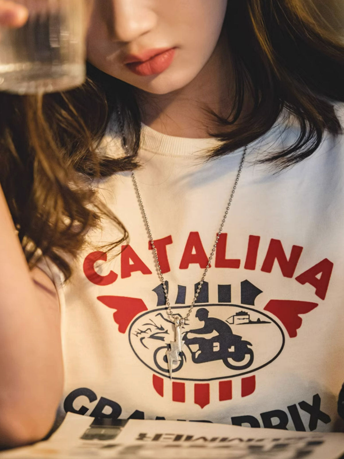 モデルがカタリナ・グランプリ モーターサイクルレースプリントTシャツを着用し、カジュアルスタイルを披露。