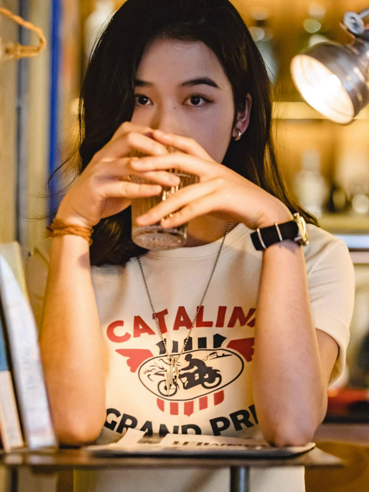 モデルがカタリナ・グランプリ モーターサイクルレースプリントTシャツを着用し、カジュアルスタイルを披露。