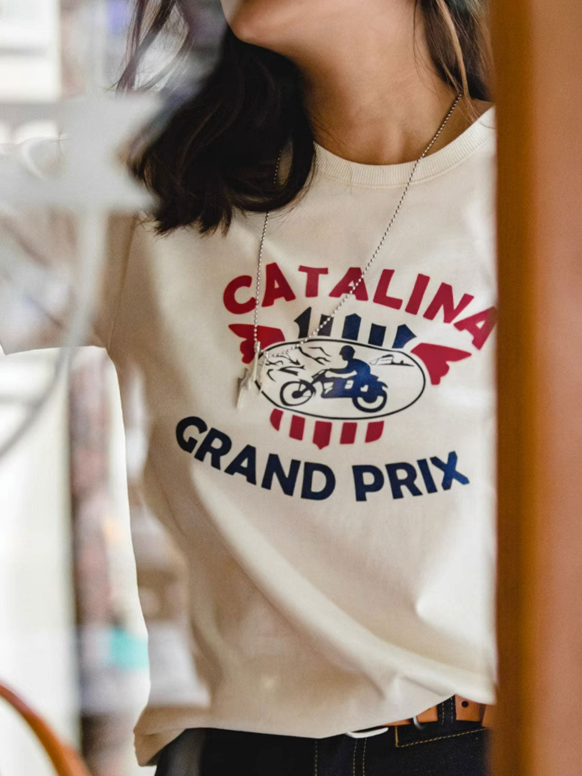 モデルがカタリナ・グランプリ モーターサイクルレースプリントTシャツを着用し、カジュアルスタイルを披露。