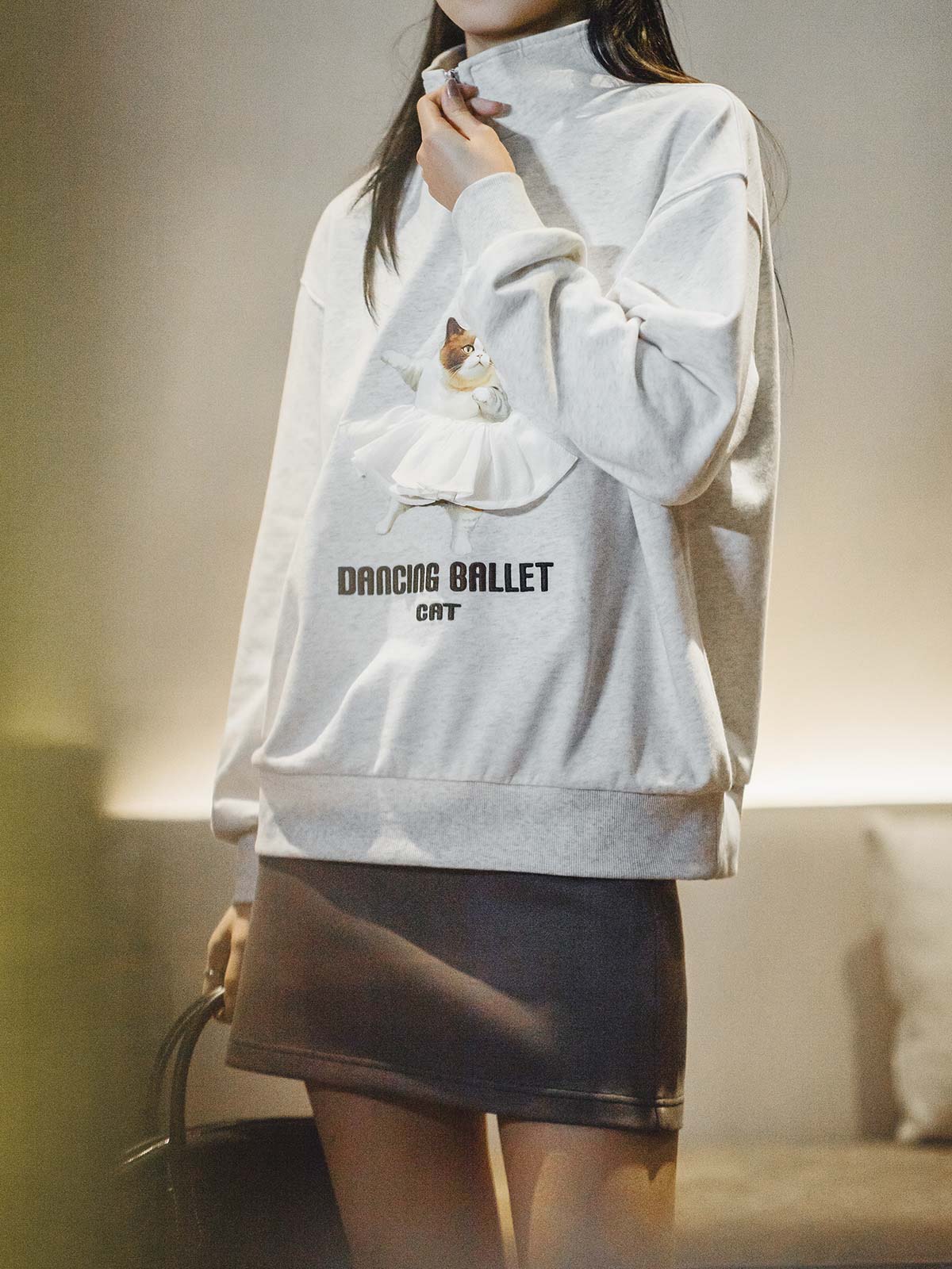 モデルがPESSOA CLUBのグレー「バレエキャット」スウェットシャツを着用し、リラックスフィットのスタンドカラーとハーフジップデザインを披露
