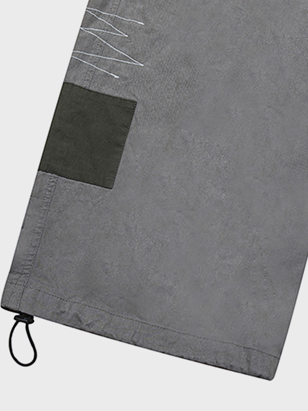 カジュアルパンツのドローコードとパッチワークディテールのクローズアップ。素材の耐久性と細部の工夫が見て取れる、機能的でスタイリッシュなデザイン。