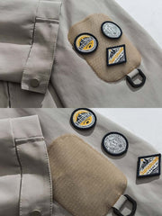 製品画像: エポレット付きフードワークジャケットの正面展示。ミリタリー風デザインと実用性を兼ね備え、防風・防水機能でアウトドアにも最適。エポレットと多機能パッチが特徴的。

詳細画像: エポレットディテールと袖口のパッチ、ドローコード付き裾の調整可能なデザインが際立つ。軽量で着やすい100%ポリエステル素材が防風・防水機能を提供。