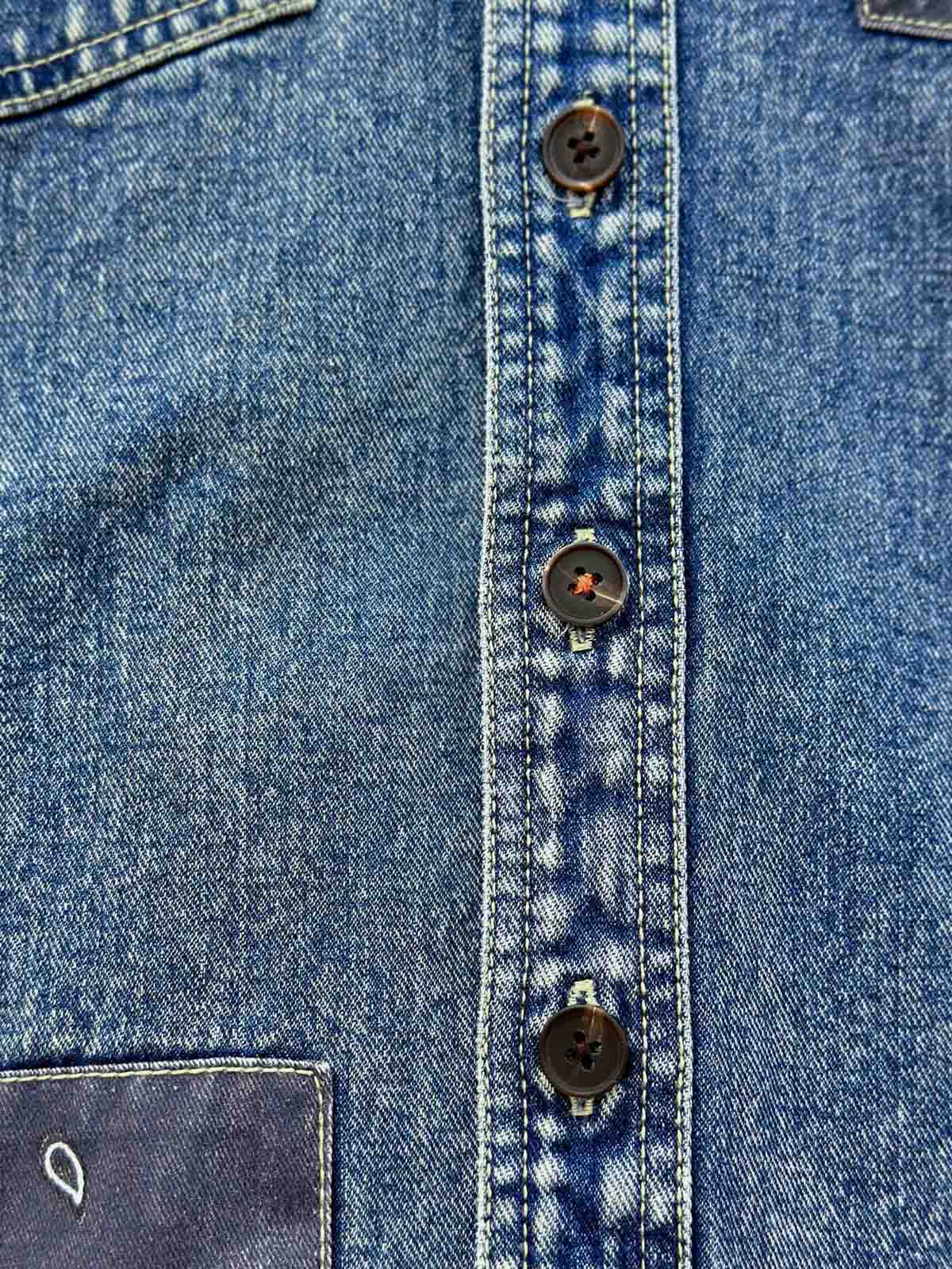 デニムシャツの袖口にあるタイスリーブノットとポケットのステッチラインのクローズアップ。手作業の細かなデテールが強調されている。