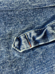 デニムシャツの袖口にあるタイスリーブノットとポケットのステッチラインのクローズアップ。手作業の細かなデテールが強調されている。