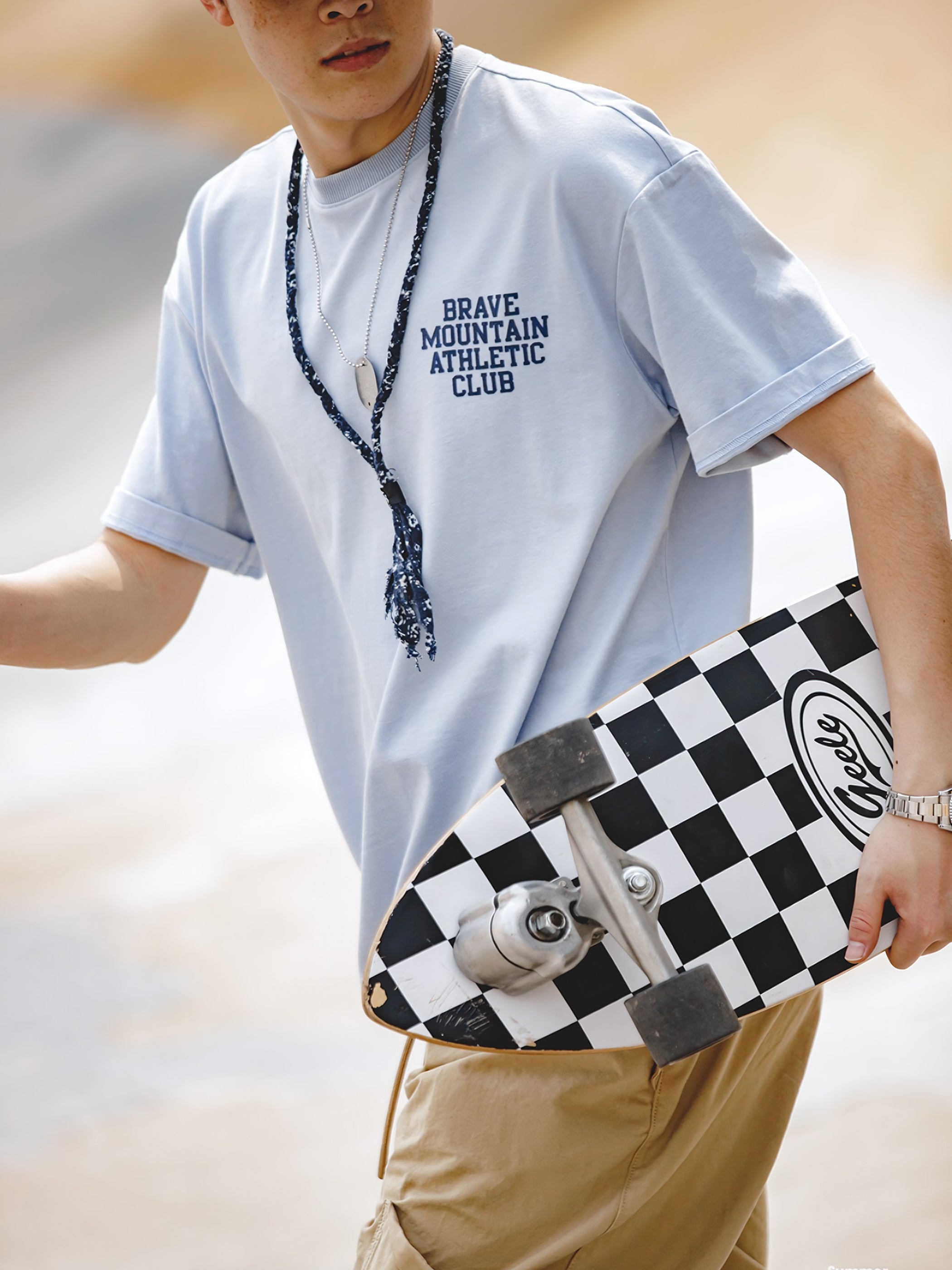 モデルが着用する「BRAVE MOUNTAIN ATHLETIC CLUB」プリントのマカロンカラーTシャツ、リラックスしつつ洗練されたフィット感を示す。