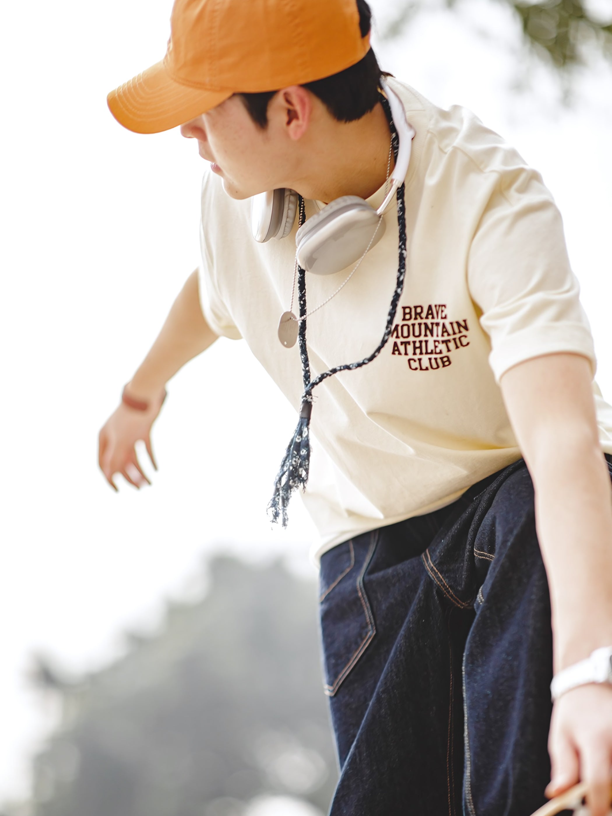 モデルが着用する「BRAVE MOUNTAIN ATHLETIC CLUB」プリントのマカロンカラーTシャツ、リラックスしつつ洗練されたフィット感を示す。