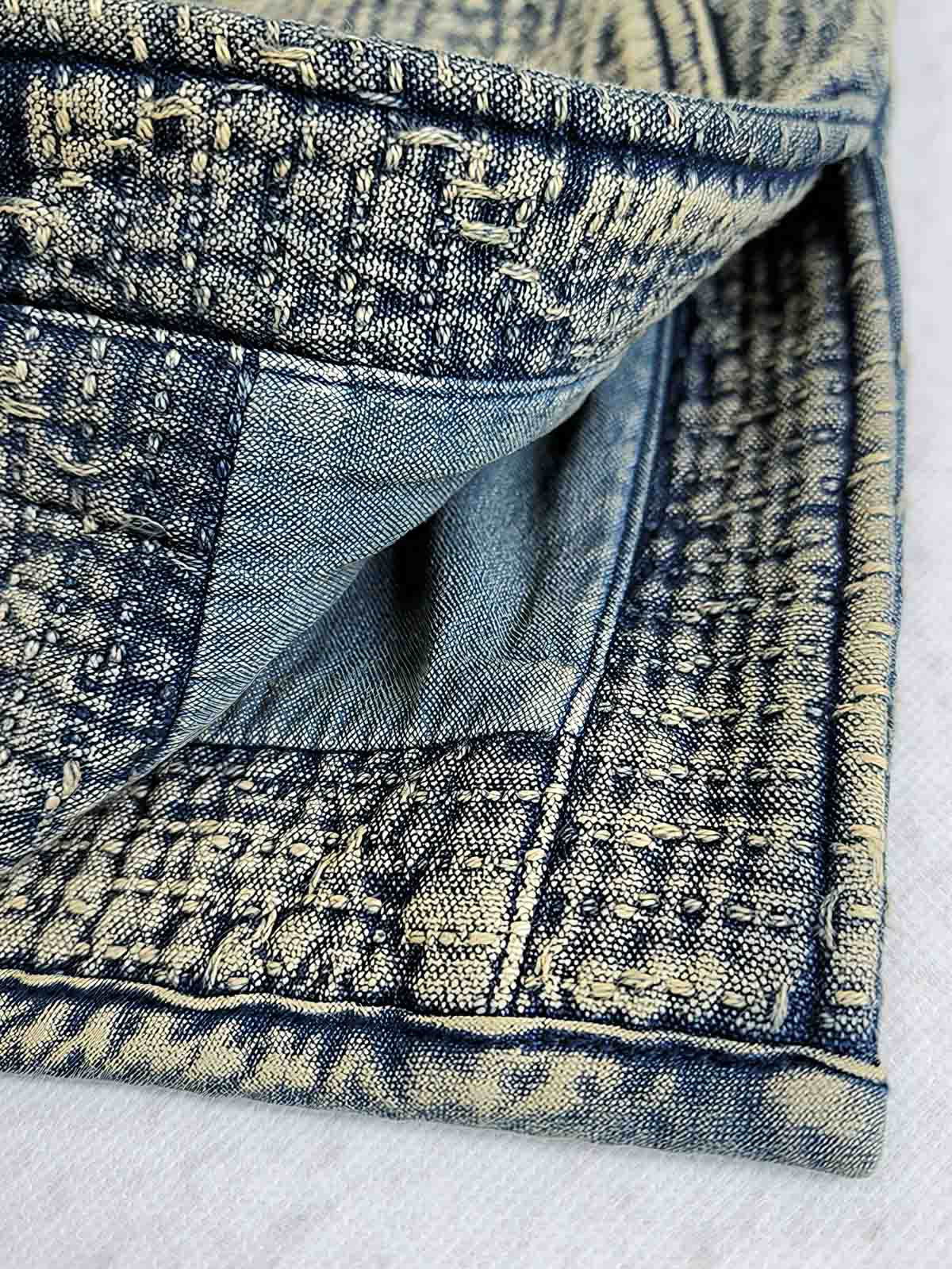 製品画像: 藍染め刺子織りピースワークスタンドカラージャケット全体写真。立ち襟とチャイナボタンが特徴の伝統とモダンが融合したデザイン。
詳細画像: 刺子織りの繊細なテクスチャと藍染めの深みある色合いを強調したディテール写真。水洗抜染加工による個性的な風合いを表現。