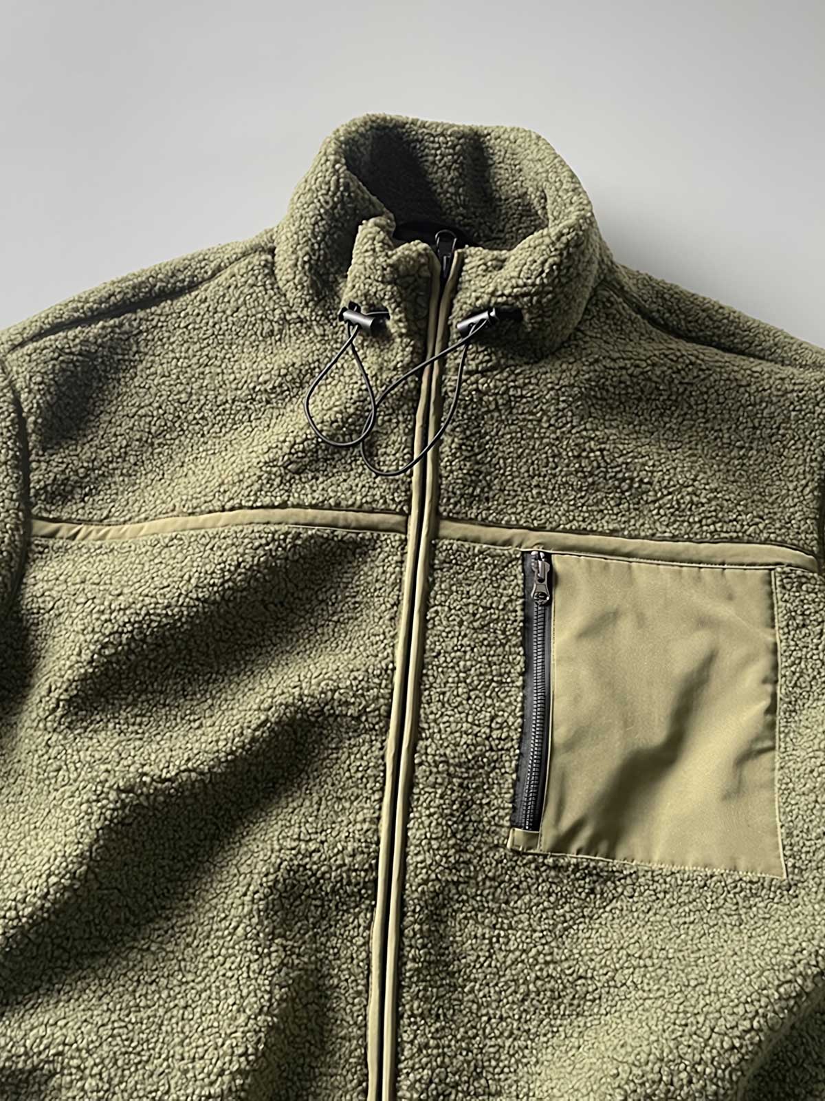 製品画像: ボアフリーススタンドカラージャケットの全体画像、アウトドアやカジュアルスタイルに対応。
詳細画像: 胸元ジッパーポケットのディテール画像、実用性とデザイン性を強調。