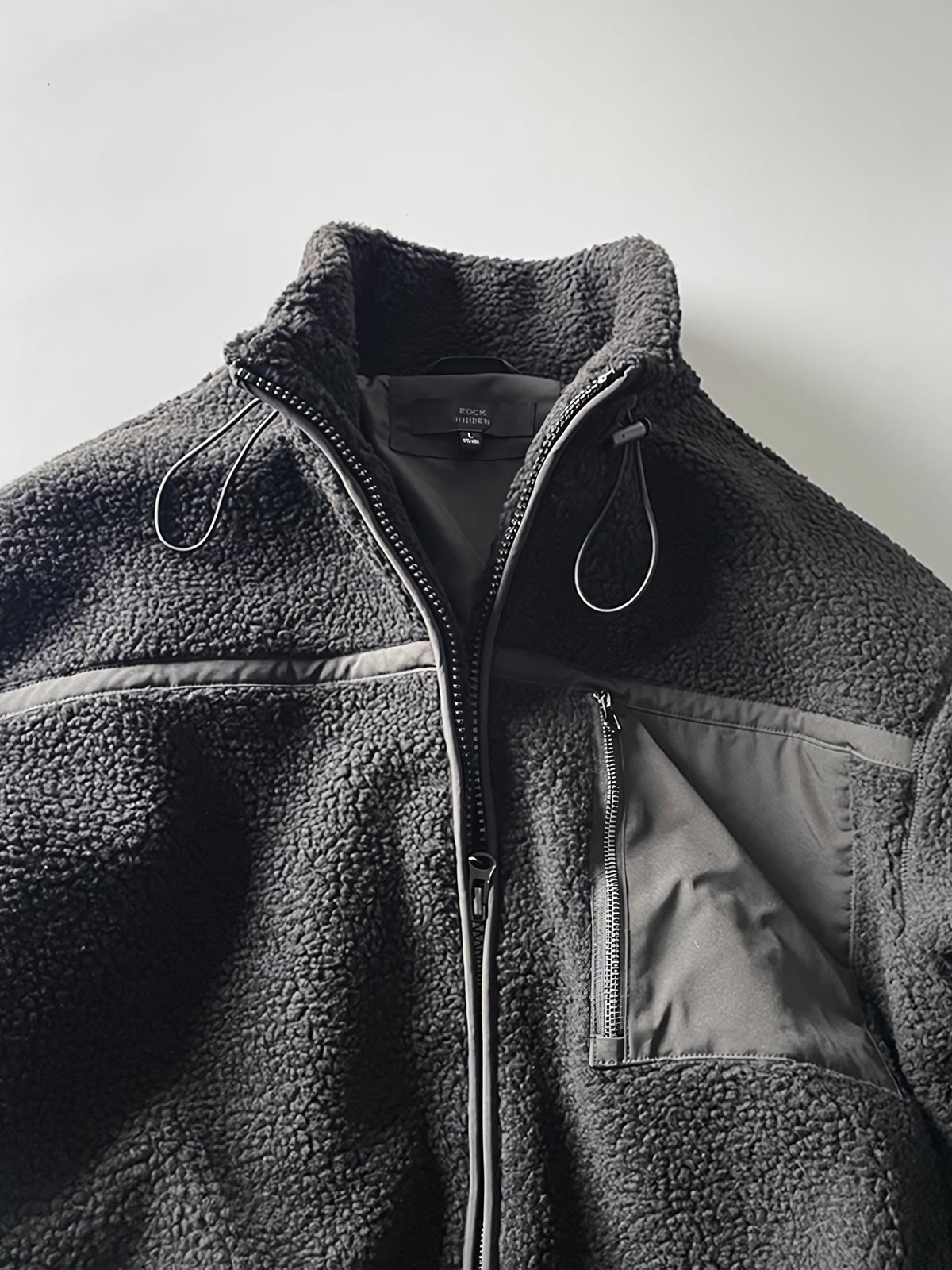 製品画像: ボアフリーススタンドカラージャケットの全体画像、アウトドアやカジュアルスタイルに対応。
詳細画像: 胸元ジッパーポケットのディテール画像、実用性とデザイン性を強調。