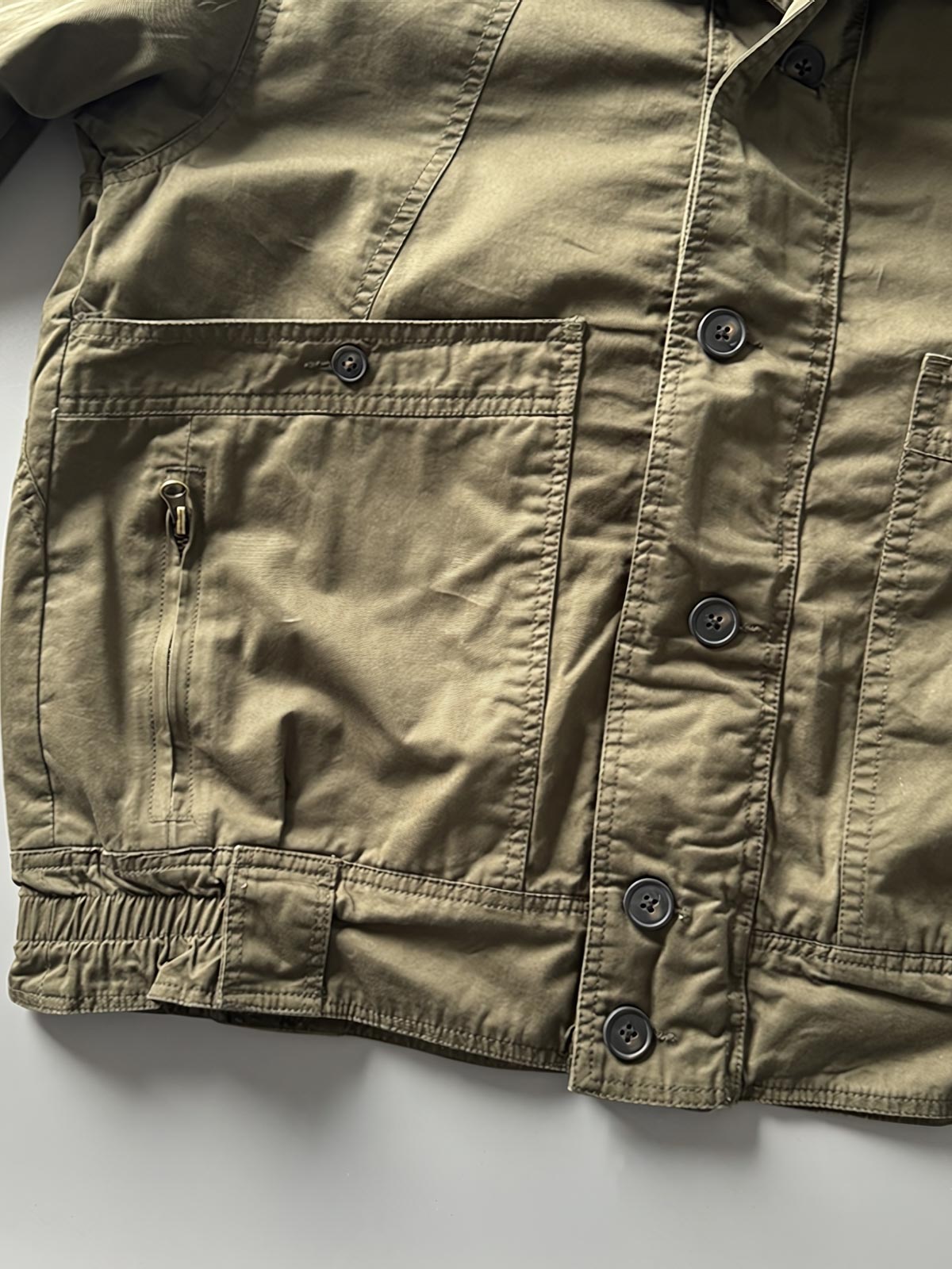 製品画像: オレンジカラーのダブルスタンドカラーワークジャケットの正面画像、実用的でスタイリッシュなデザインが特徴。
詳細画像: 袖部のジッパーポケットとスタンドカラーデザインのディテール画像、ワークスタイルを強調。