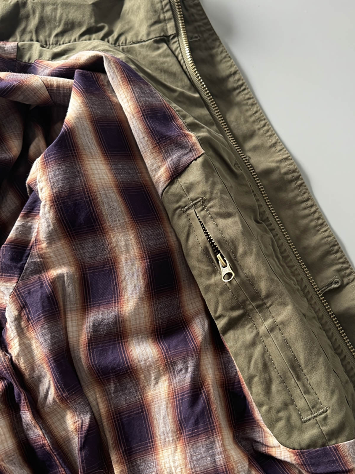 製品画像: オレンジカラーのダブルスタンドカラーワークジャケットの正面画像、実用的でスタイリッシュなデザインが特徴。
詳細画像: 袖部のジッパーポケットとスタンドカラーデザインのディテール画像、ワークスタイルを強調。