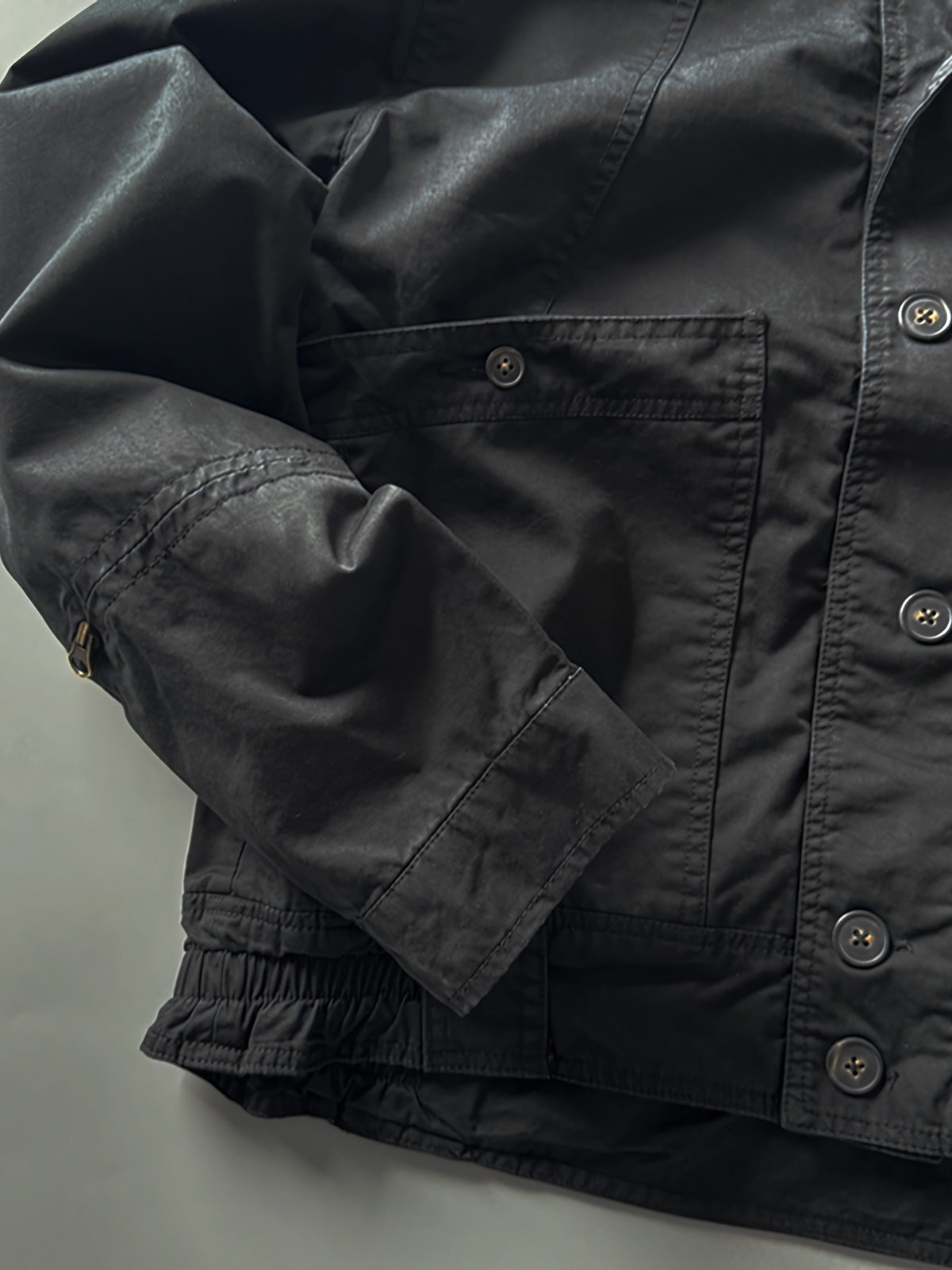 製品画像: オレンジカラーのダブルスタンドカラーワークジャケットの正面画像、実用的でスタイリッシュなデザインが特徴。
詳細画像: 袖部のジッパーポケットとスタンドカラーデザインのディテール画像、ワークスタイルを強調。