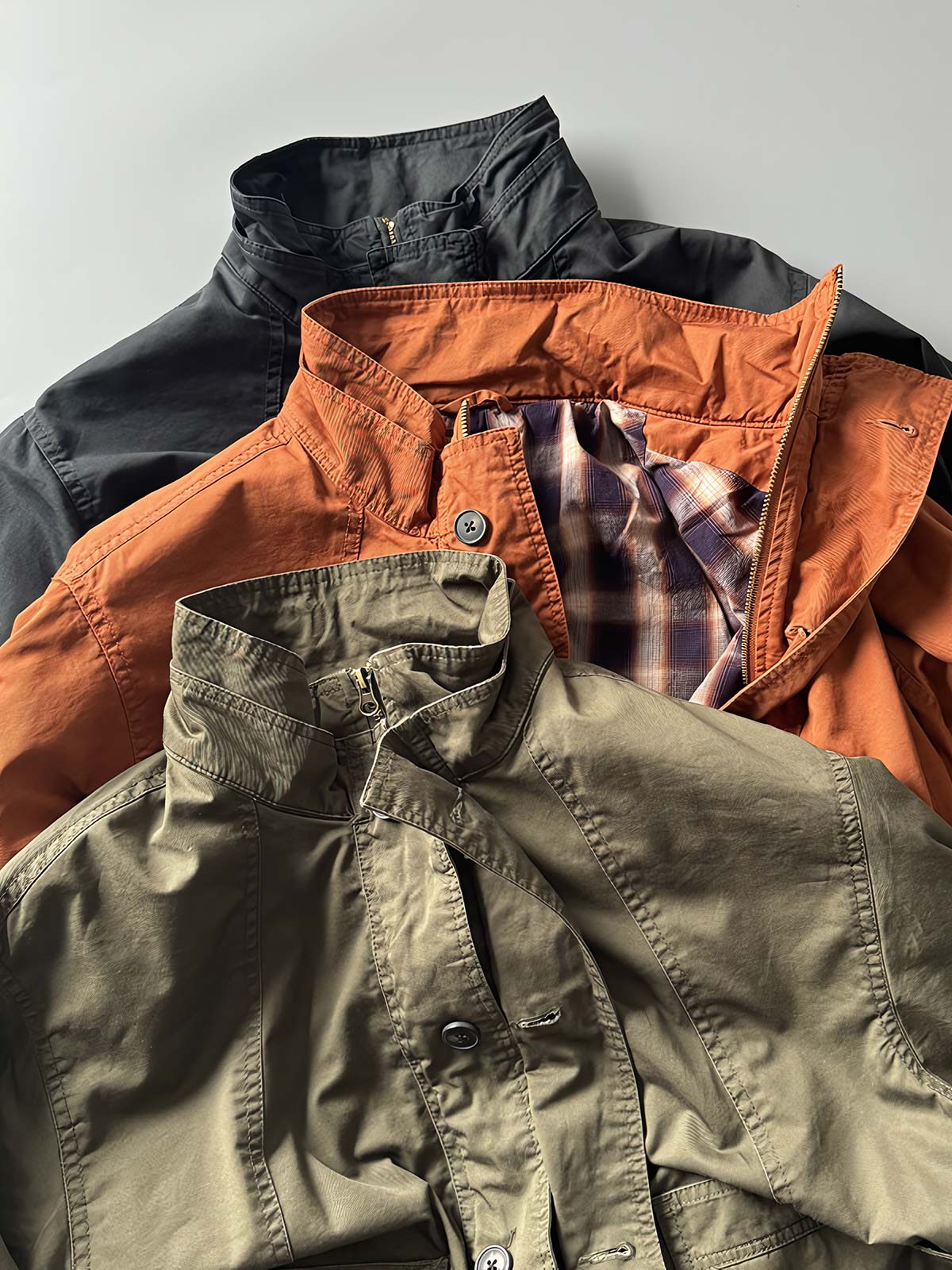 製品画像: オレンジカラーのダブルスタンドカラーワークジャケットの正面画像、実用的でスタイリッシュなデザインが特徴。
詳細画像: 袖部のジッパーポケットとスタンドカラーデザインのディテール画像、ワークスタイルを強調。