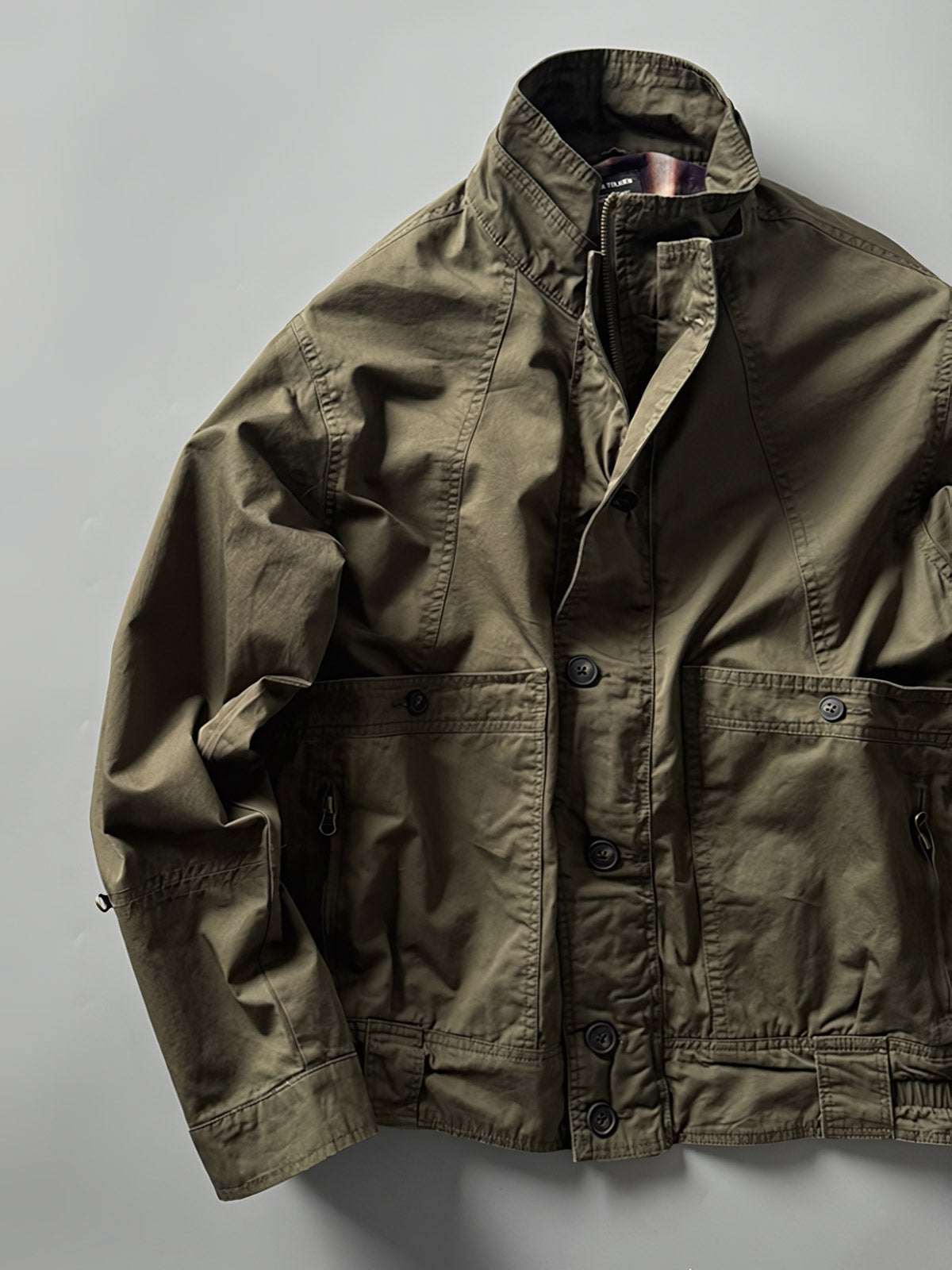 製品画像: オレンジカラーのダブルスタンドカラーワークジャケットの正面画像、実用的でスタイリッシュなデザインが特徴。
詳細画像: 袖部のジッパーポケットとスタンドカラーデザインのディテール画像、ワークスタイルを強調。