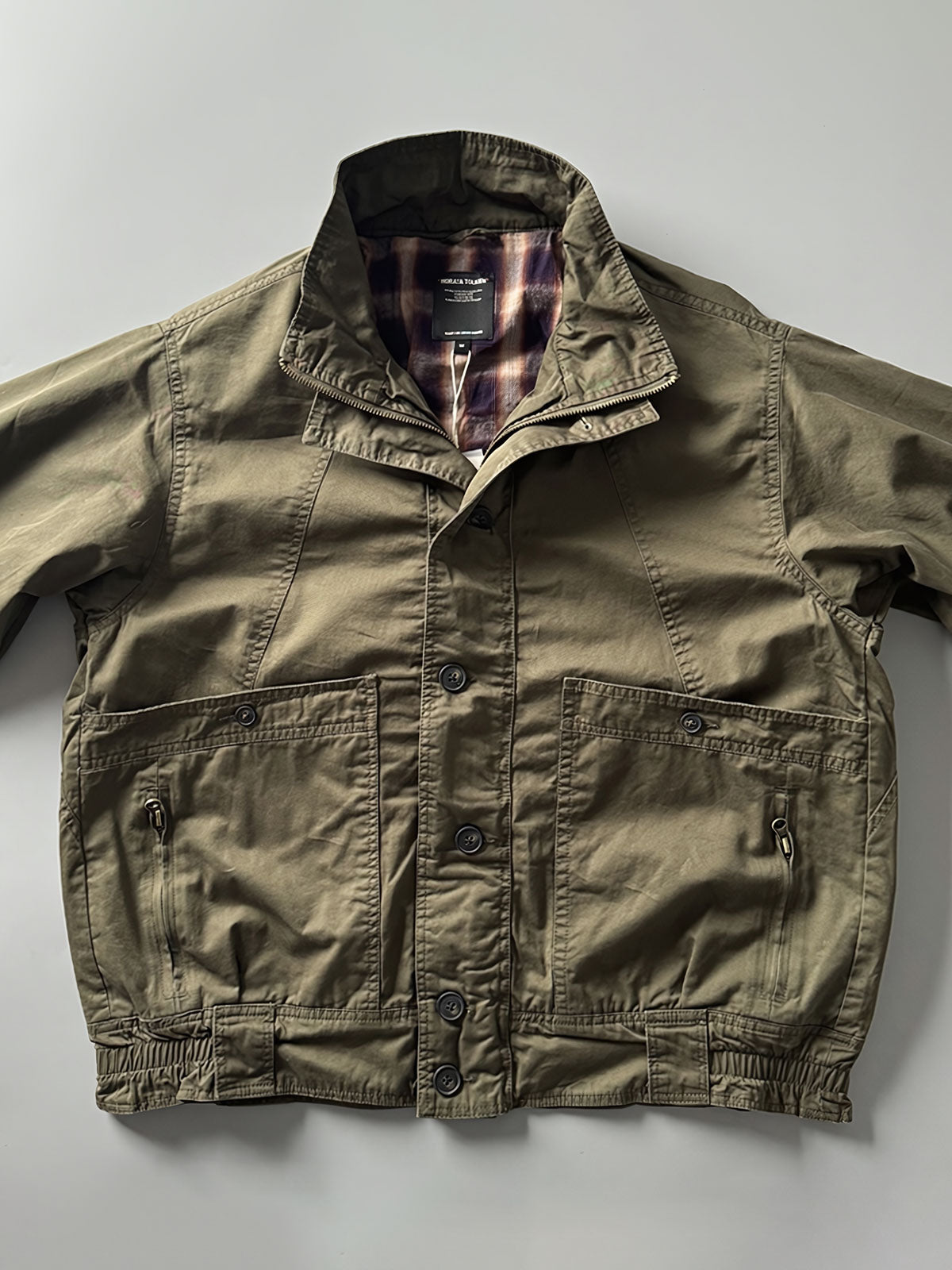 製品画像: オレンジカラーのダブルスタンドカラーワークジャケットの正面画像、実用的でスタイリッシュなデザインが特徴。
詳細画像: 袖部のジッパーポケットとスタンドカラーデザインのディテール画像、ワークスタイルを強調。