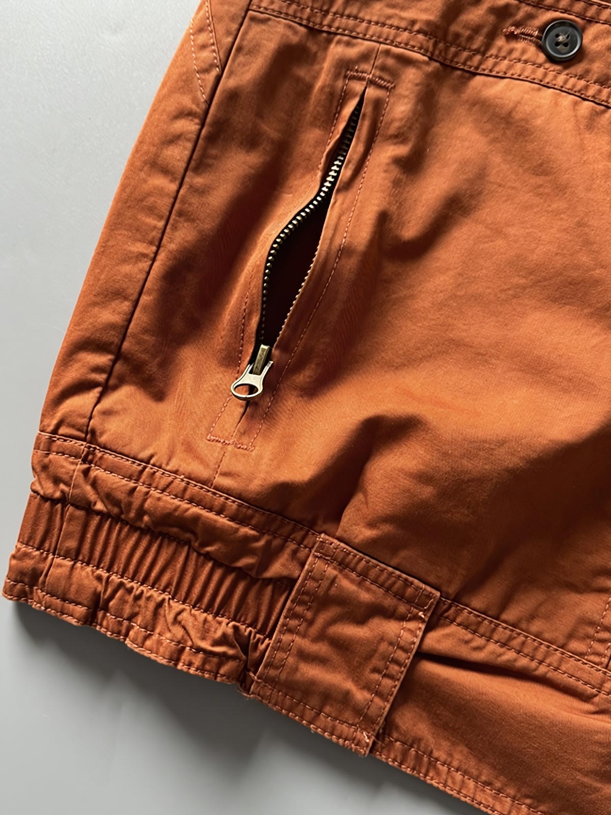 製品画像: オレンジカラーのダブルスタンドカラーワークジャケットの正面画像、実用的でスタイリッシュなデザインが特徴。
詳細画像: 袖部のジッパーポケットとスタンドカラーデザインのディテール画像、ワークスタイルを強調。