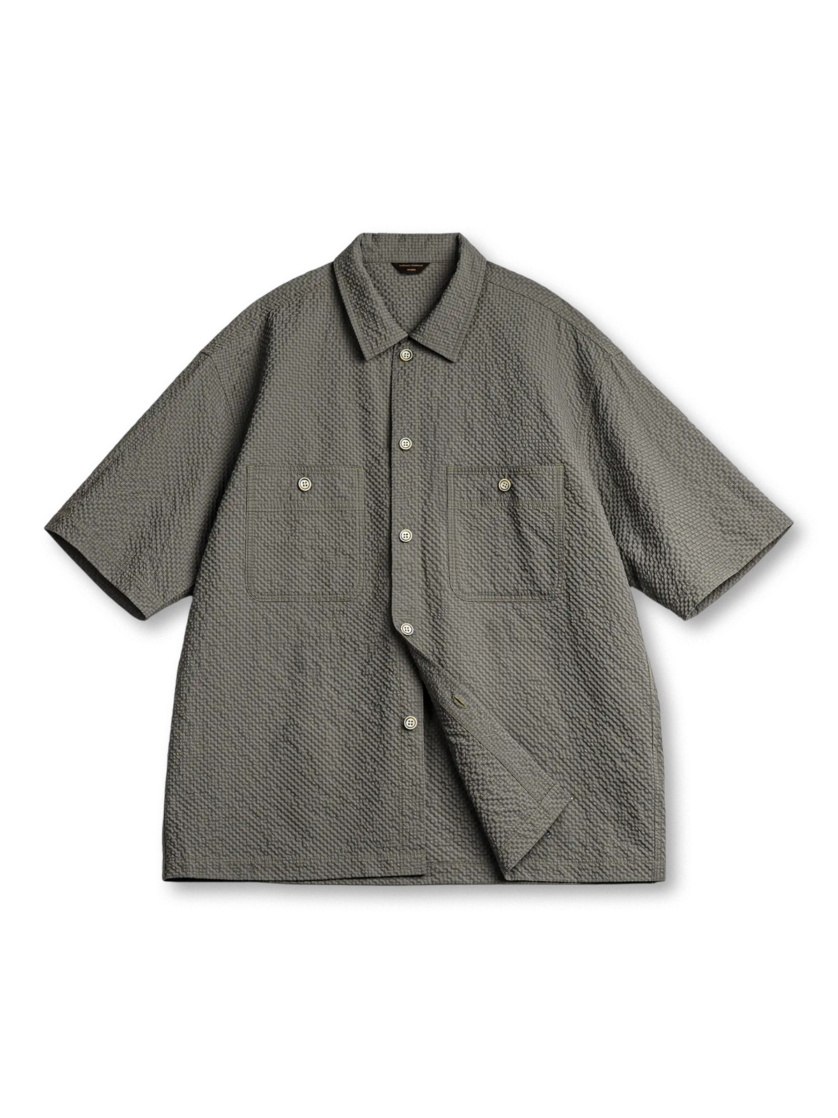 軽量シアサッカー生地を使用した2ポケットワークシャツ。小さめ襟と5ボタン仕様、背面にレーザー木製プレートと琥珀ボタンがアクセントの涼しげでモダンなデザイン。