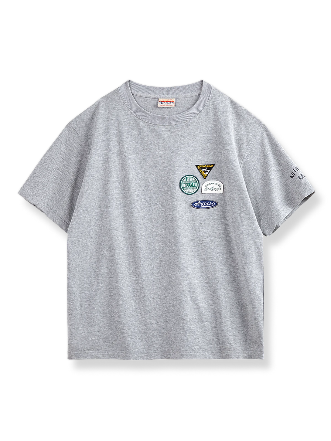 左胸に4つのカラフルな刺繍バッジが付いたグレーベースの半袖Tシャツ。