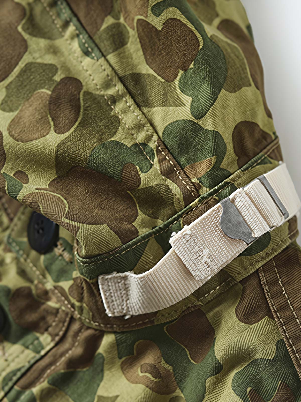 製品画像: 迷彩柄ツイルデニム生地の砲兵防護プルオーバーパーカー復刻バージョンの正面画像。
詳細画像: 大きなフードと三層前立てデザインのディテール特写。機能性とヴィンテージ感が際立つディテール。
