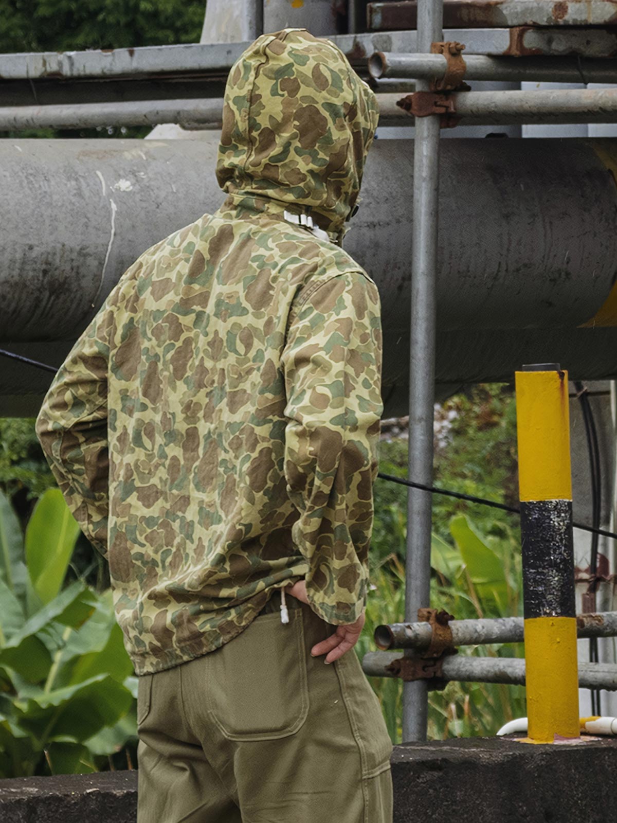 詳細画像: 大きなフードと三層前立てデザインのディテール特写。機能性とヴィンテージ感が際立つディテール。
モデル画像: モデルが迷彩柄砲兵防護プルオーバーパーカーを着用したスタイリング例。戦時風デザインを取り入れたコーディネート。