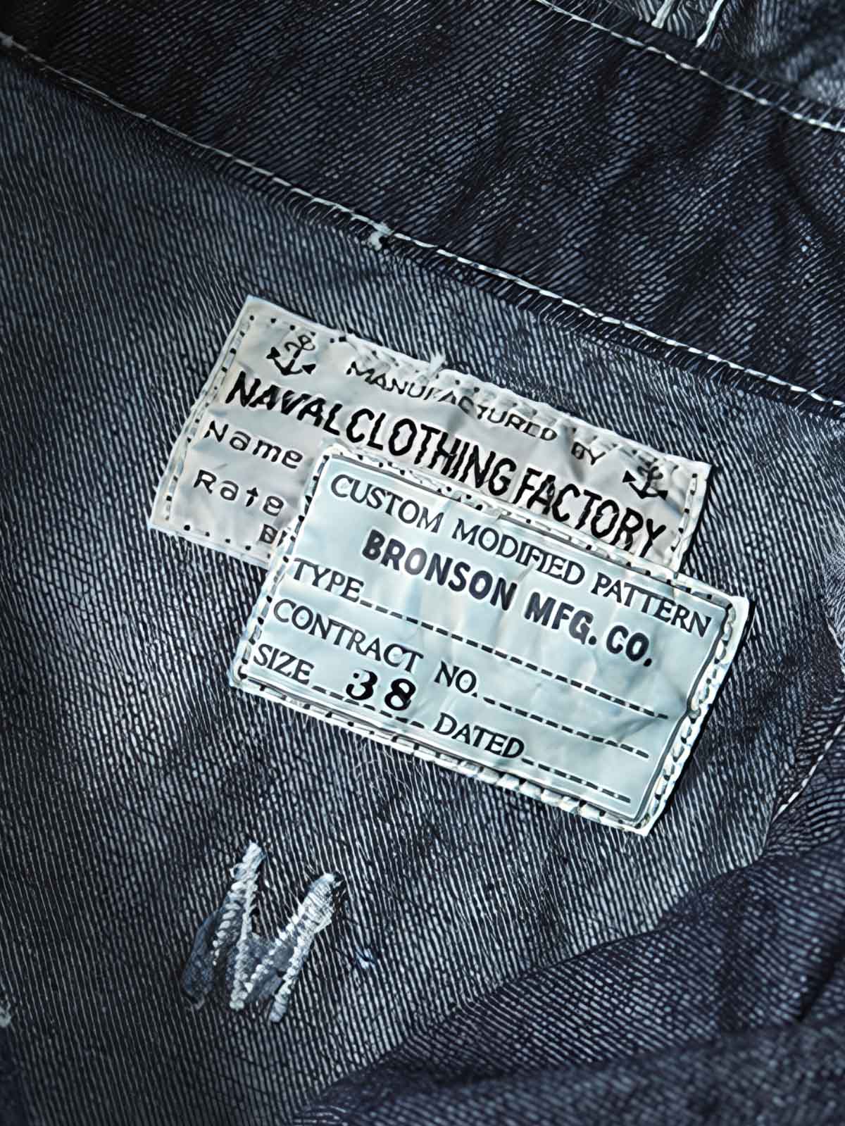 製品画像: 迷彩柄ツイルデニム生地の砲兵防護プルオーバーパーカー復刻バージョンの正面画像。
詳細画像: 大きなフードと三層前立てデザインのディテール特写。機能性とヴィンテージ感が際立つディテール。