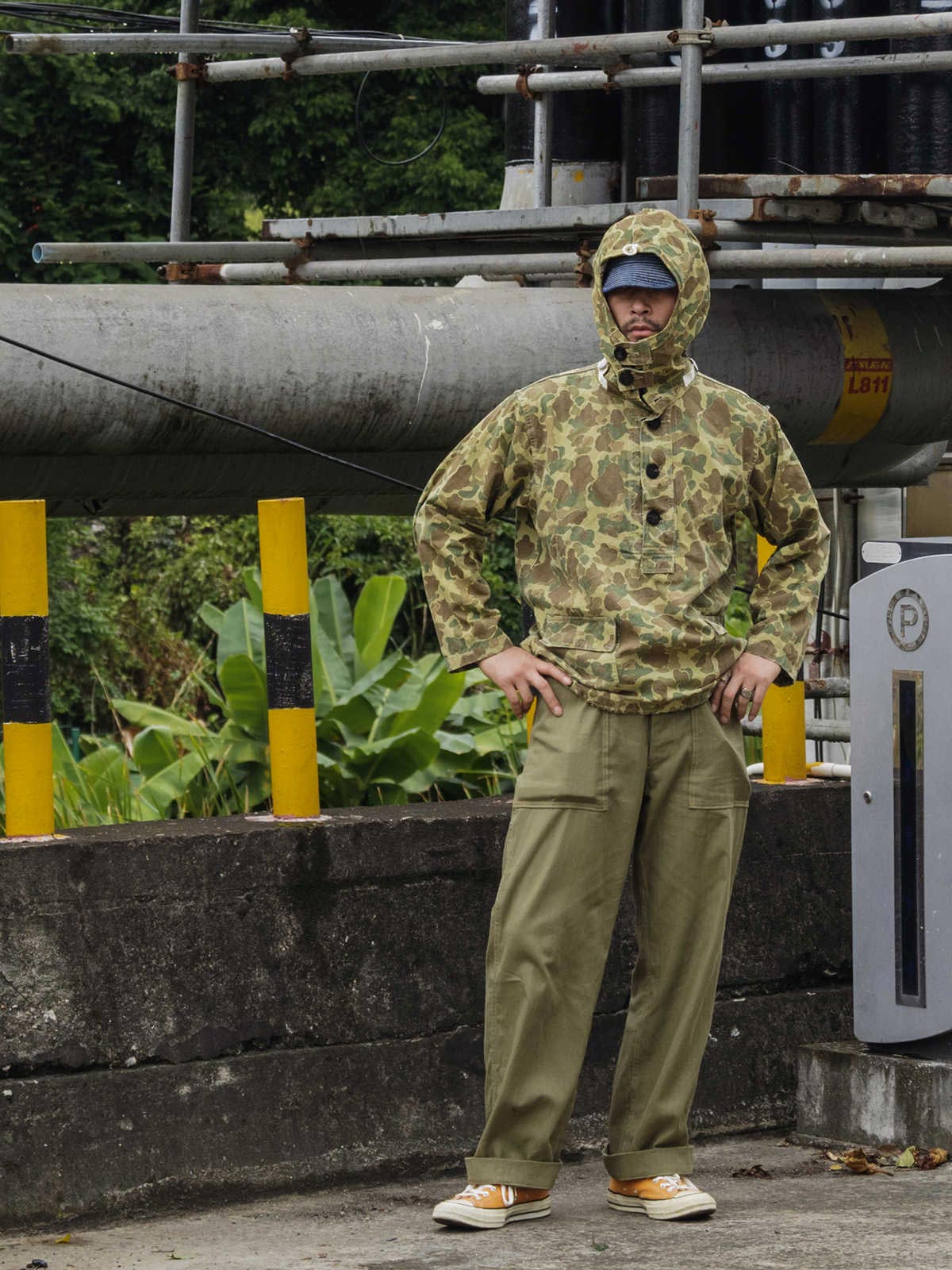詳細画像: 大きなフードと三層前立てデザインのディテール特写。機能性とヴィンテージ感が際立つディテール。
モデル画像: モデルが迷彩柄砲兵防護プルオーバーパーカーを着用したスタイリング例。戦時風デザインを取り入れたコーディネート。