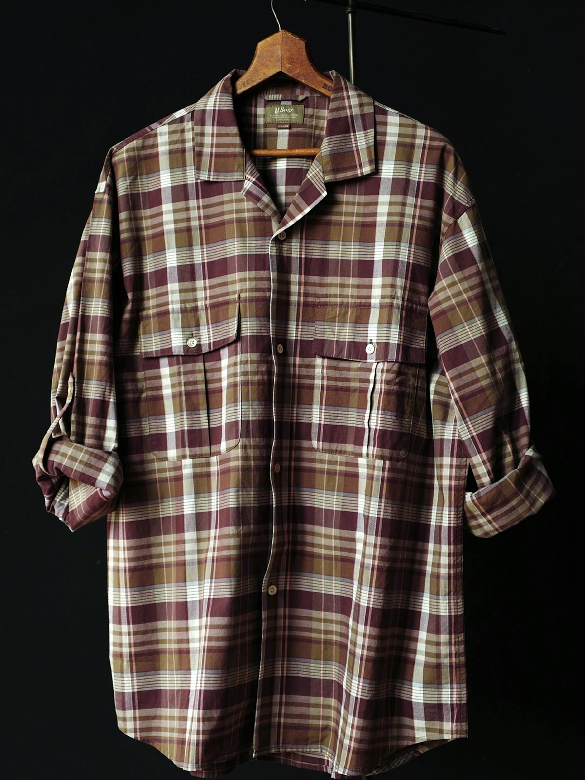 詳細画像: キューバンカラーと胸前のフラップポケットのディテール。チェック柄の鮮明さとシャツの質感を強調。
モデル画像: モデルがMADRAS (マドラス) チェック柄シャツを着用したスタイリング例。実際の着用感やフィット感を視覚的に伝える。