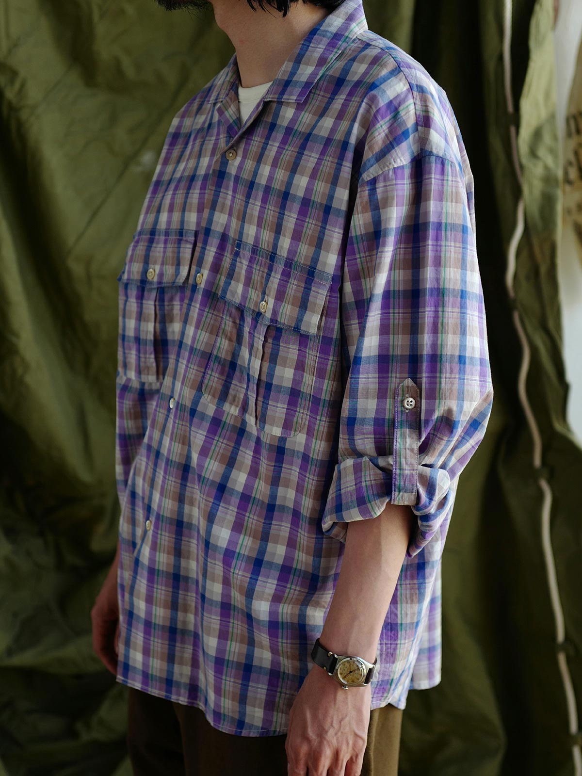 詳細画像: キューバンカラーと胸前のフラップポケットのディテール。チェック柄の鮮明さとシャツの質感を強調。
モデル画像: モデルがMADRAS (マドラス) チェック柄シャツを着用したスタイリング例。実際の着用感やフィット感を視覚的に伝える。