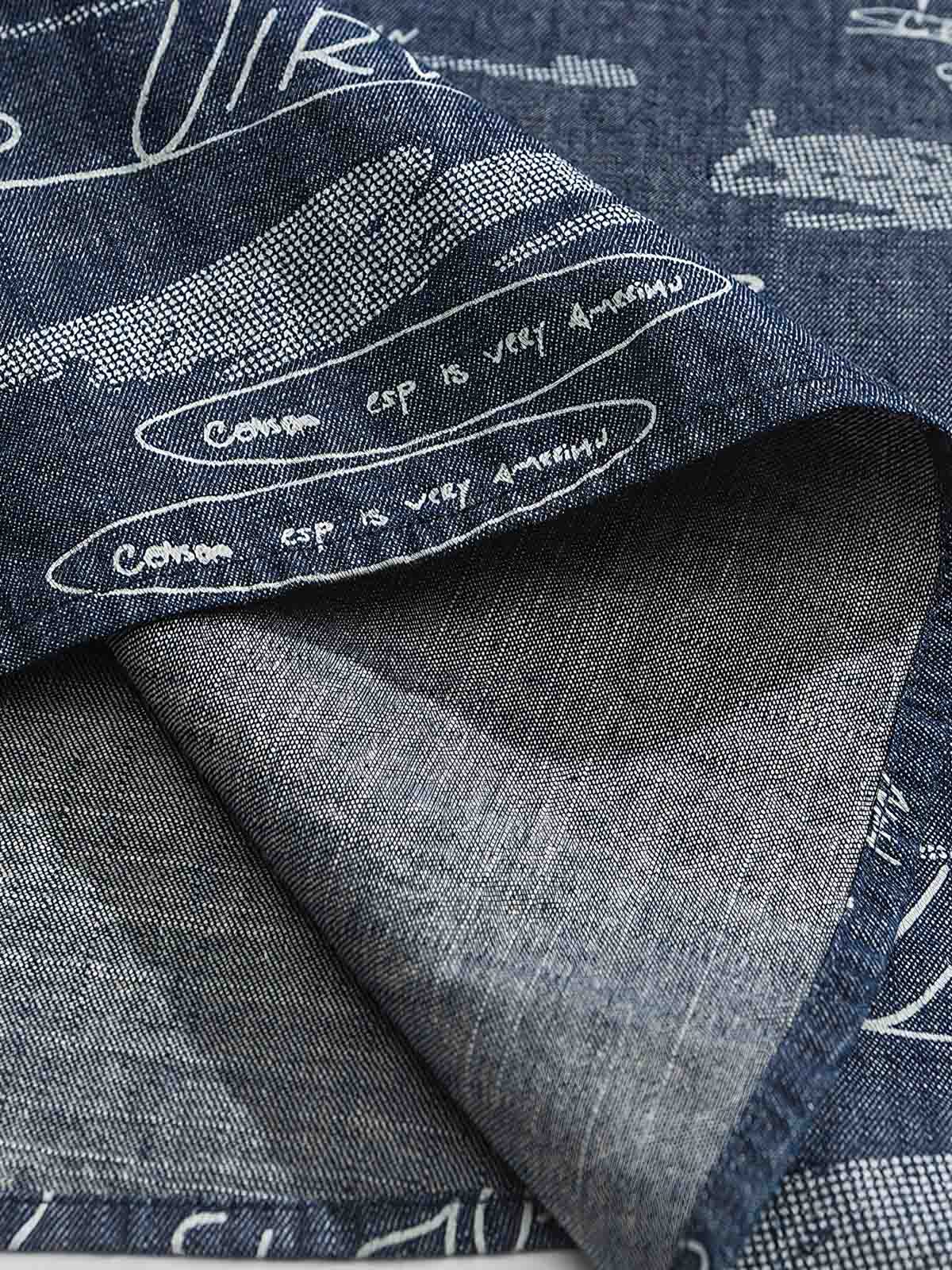 デニム半袖シャツの文字プリントディテール。厳選されたデニム素材と高品質なウォッシュ加工が施され、洗練された外見と耐久性を実現しています。