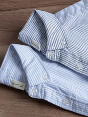 製品画像: クラシックブルーストライプオックスフォードシャツの正面展示 詳細画像: ストライプ柄と胸ポケットのデザイン詳細