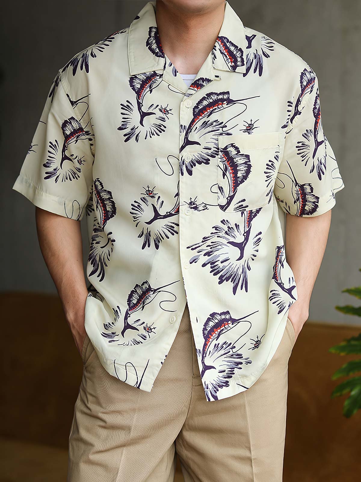 モデルがカジキプリントのハワイアンシャツを着用し、リラックスした夏のスタイリングを展示しています。