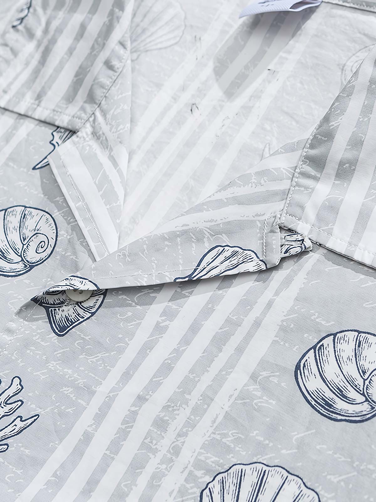 貝殻プリント半袖シャツの精巧なプリントパターンのクローズアップ。繊細な工芸技術と高品質の純綿素材が、快適な着用体験を実現します。